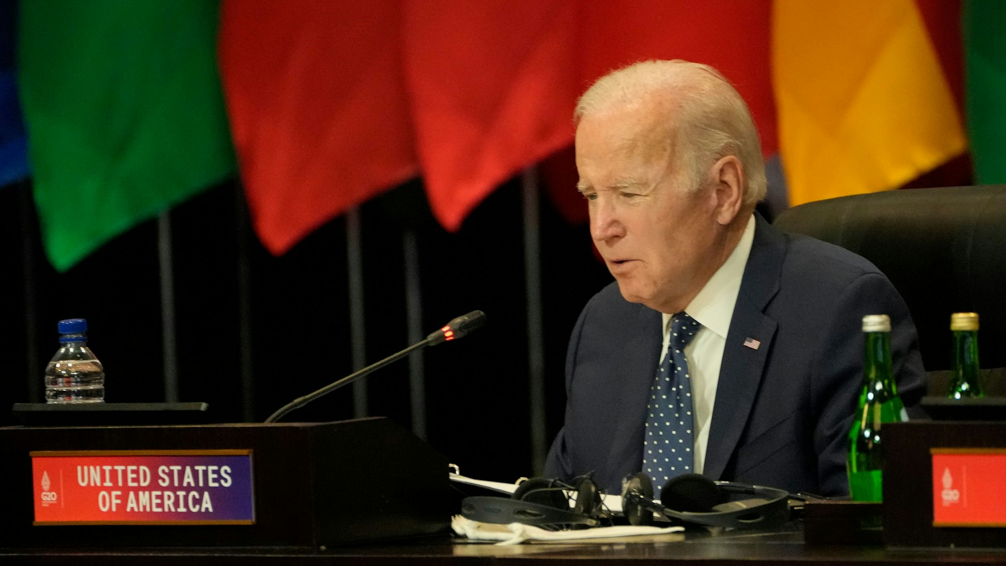 Das Foto zeigt den US-Präsident Joe Biden während des G20-Gipfels. Er spricht in ein Mikrofon, hinter ihm befinden sich Flaggen.
