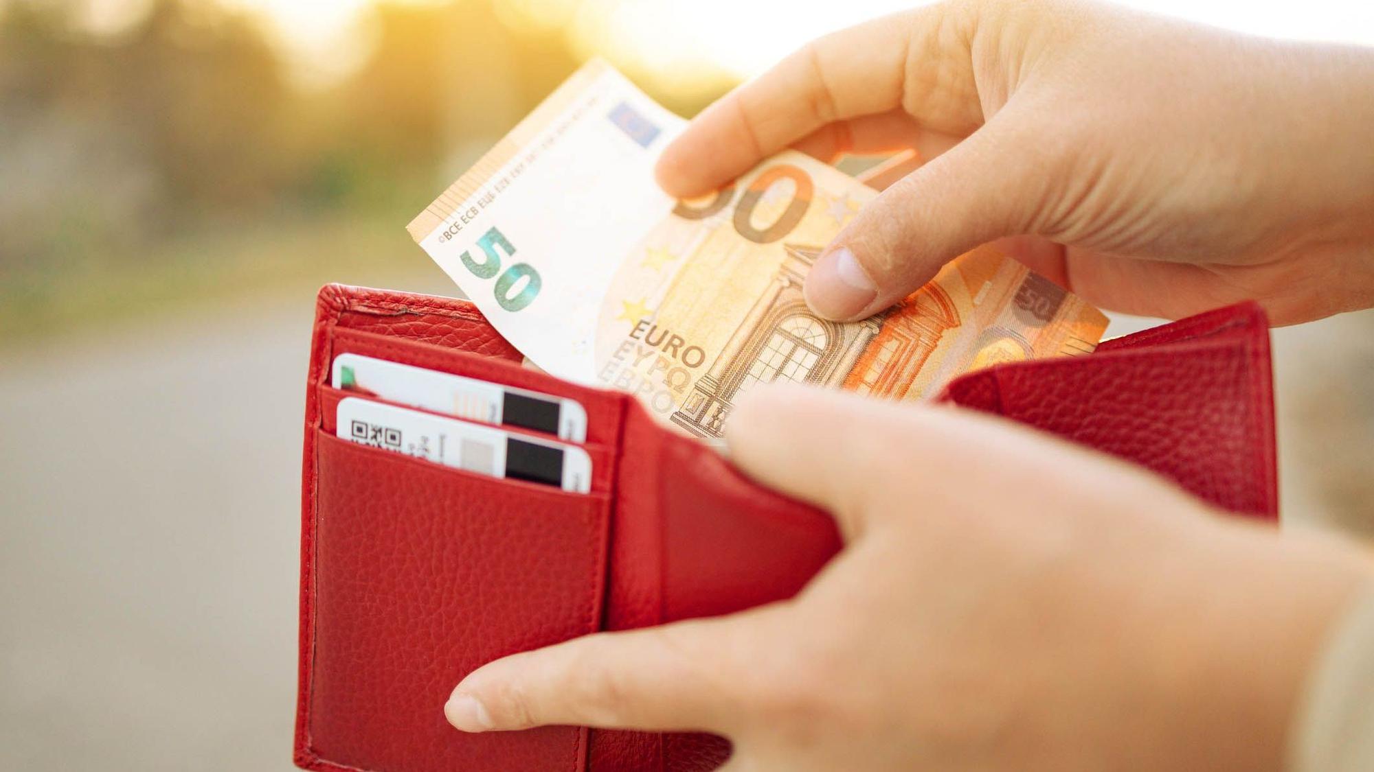 Eine Frau steckt einen 50-Euro-Schein in eine Geldbörse.