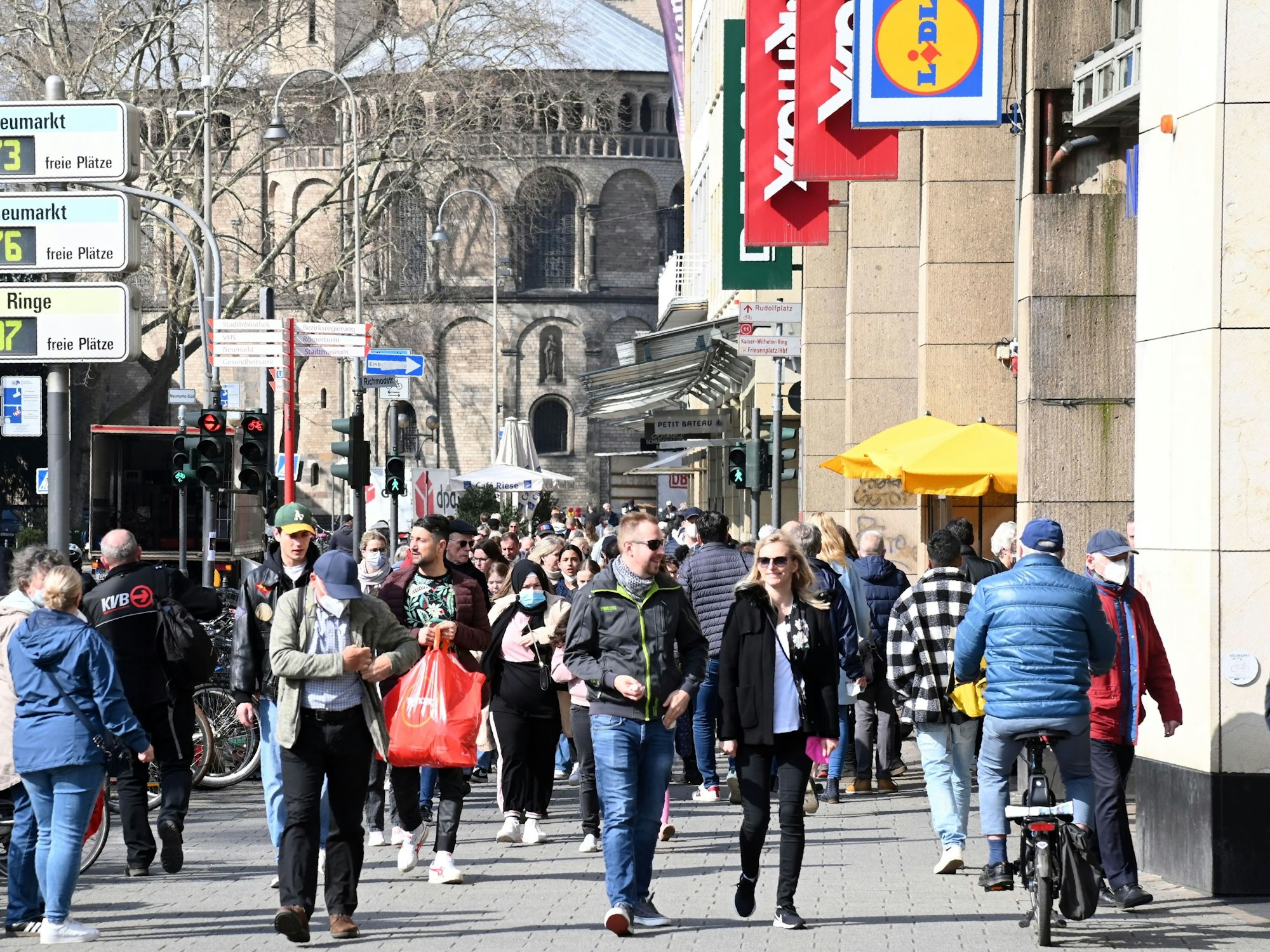 Menschen gehen am Neumarkt in Köln an Geschäften entlang und steuern auf die Schildergasse zu.