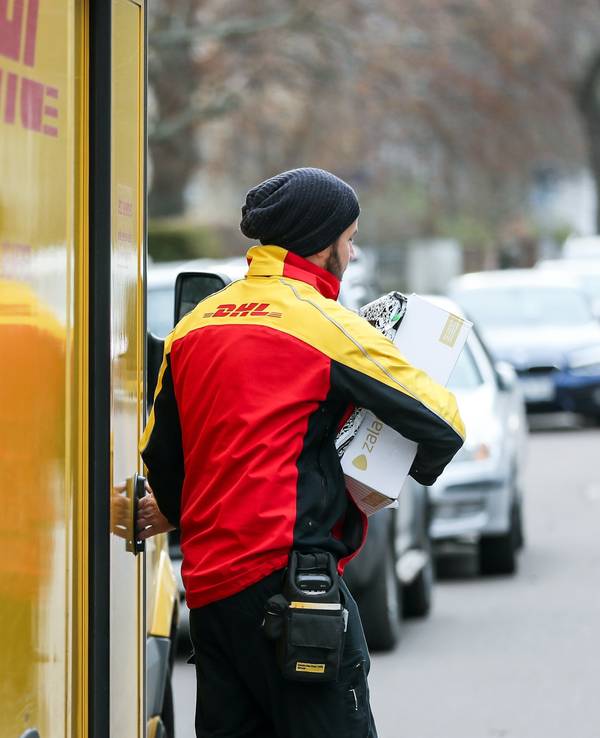 Ein DHL-Paketzusteller verlässt mit mehreren Sendungen sein Fahrzeug.