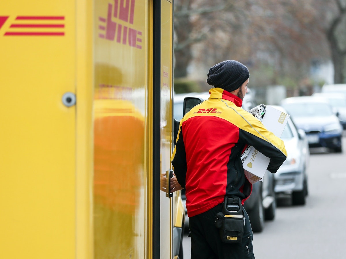 Ein DHL-Paketzusteller verlässt mit mehreren Sendungen sein Fahrzeug.