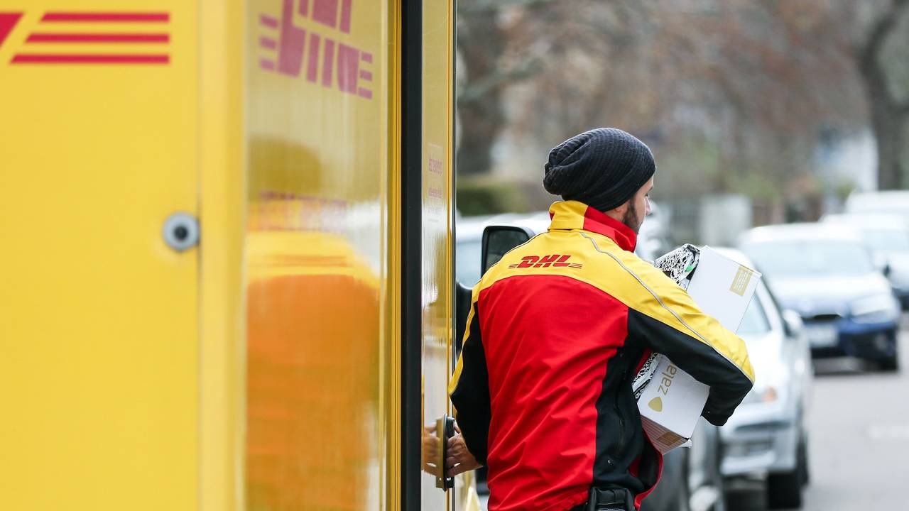Ein DHL-Paketzusteller verlässt mit mehreren Sendungen sein Fahrzeug.