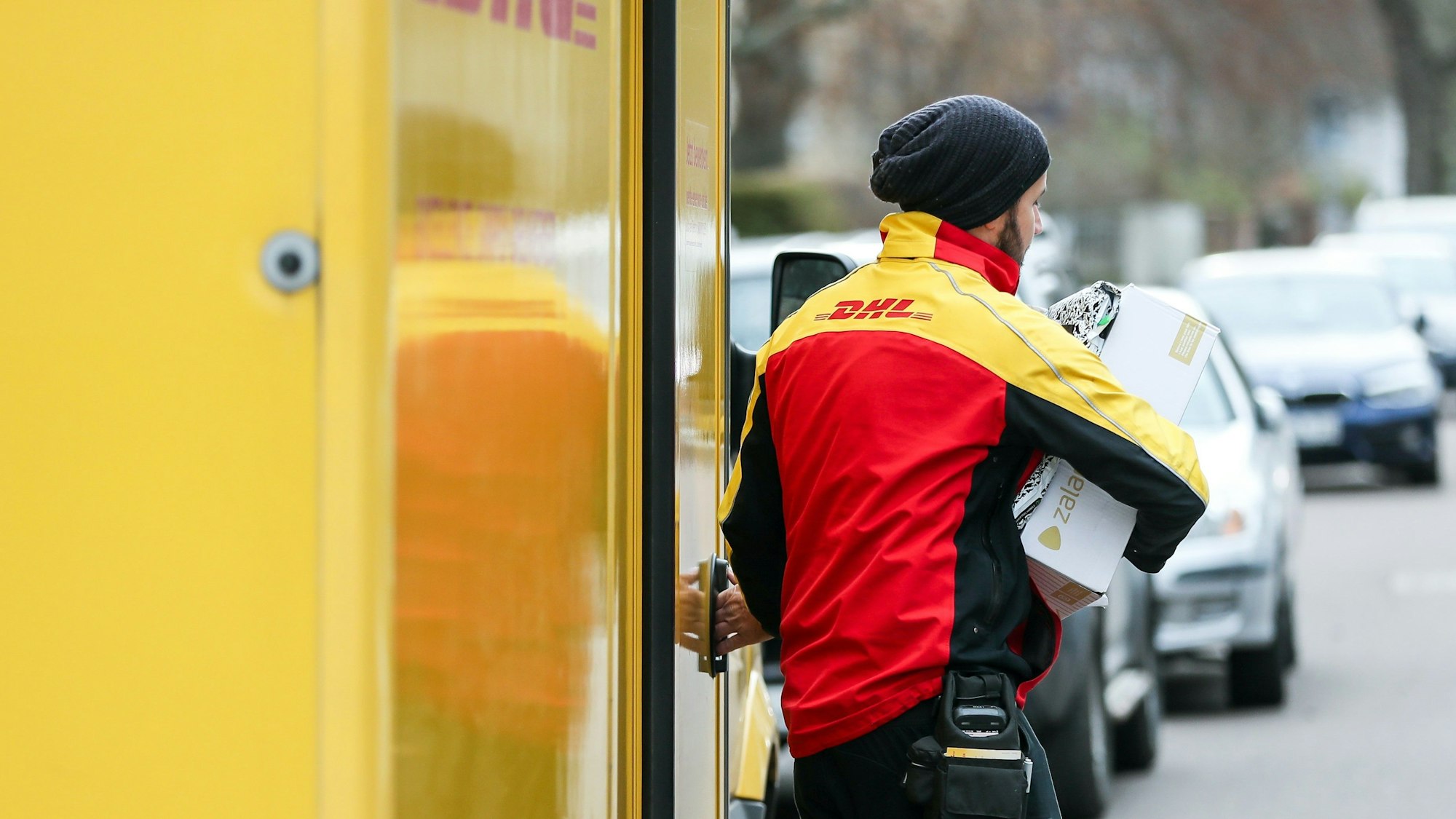 Ein DHL-Paketzusteller verlässt mit mehreren Sendungen sein Fahrzeug.