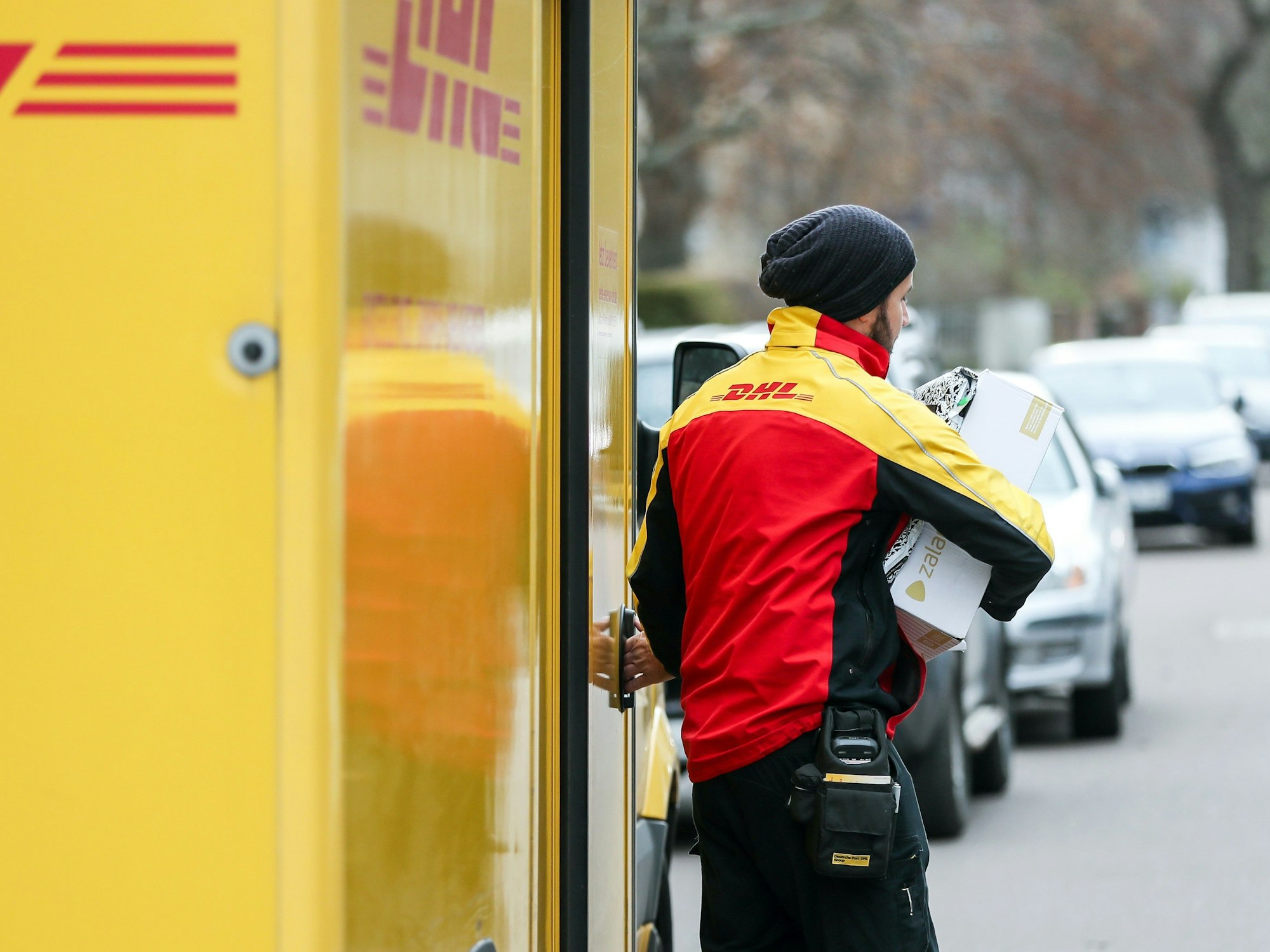 Ein DHL-Paketzusteller verlässt mit mehreren Sendungen sein Fahrzeug.