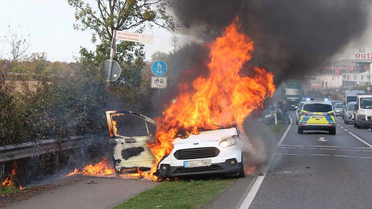 Hohe Flammen schlagen aus einem Auto, das direkt an einer Straße steht.