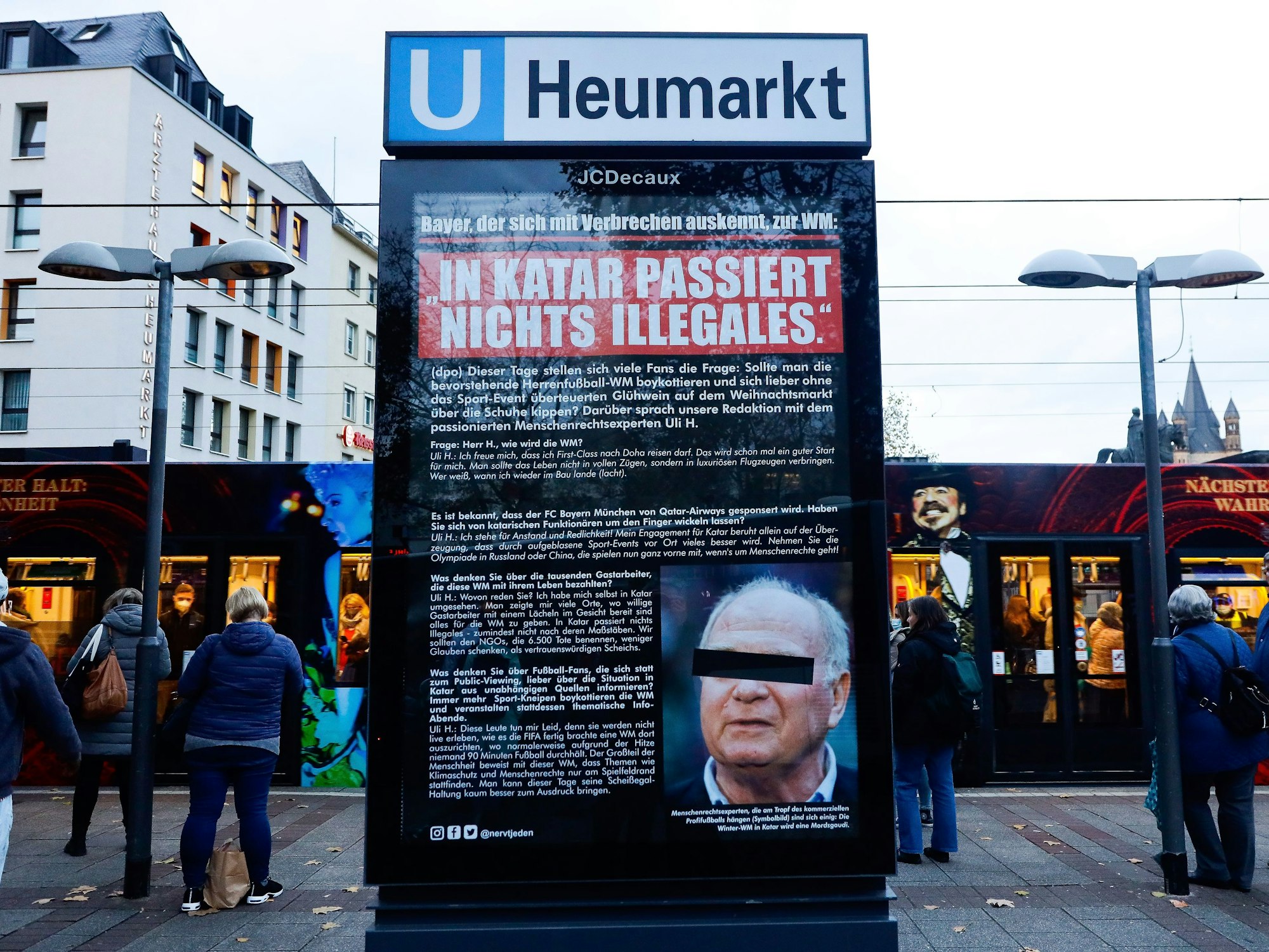 Plakat mit Foto und Aussagen von Uli Hoeneß am Neumarkt in Köln. Viele Menschen stehen drum herum.