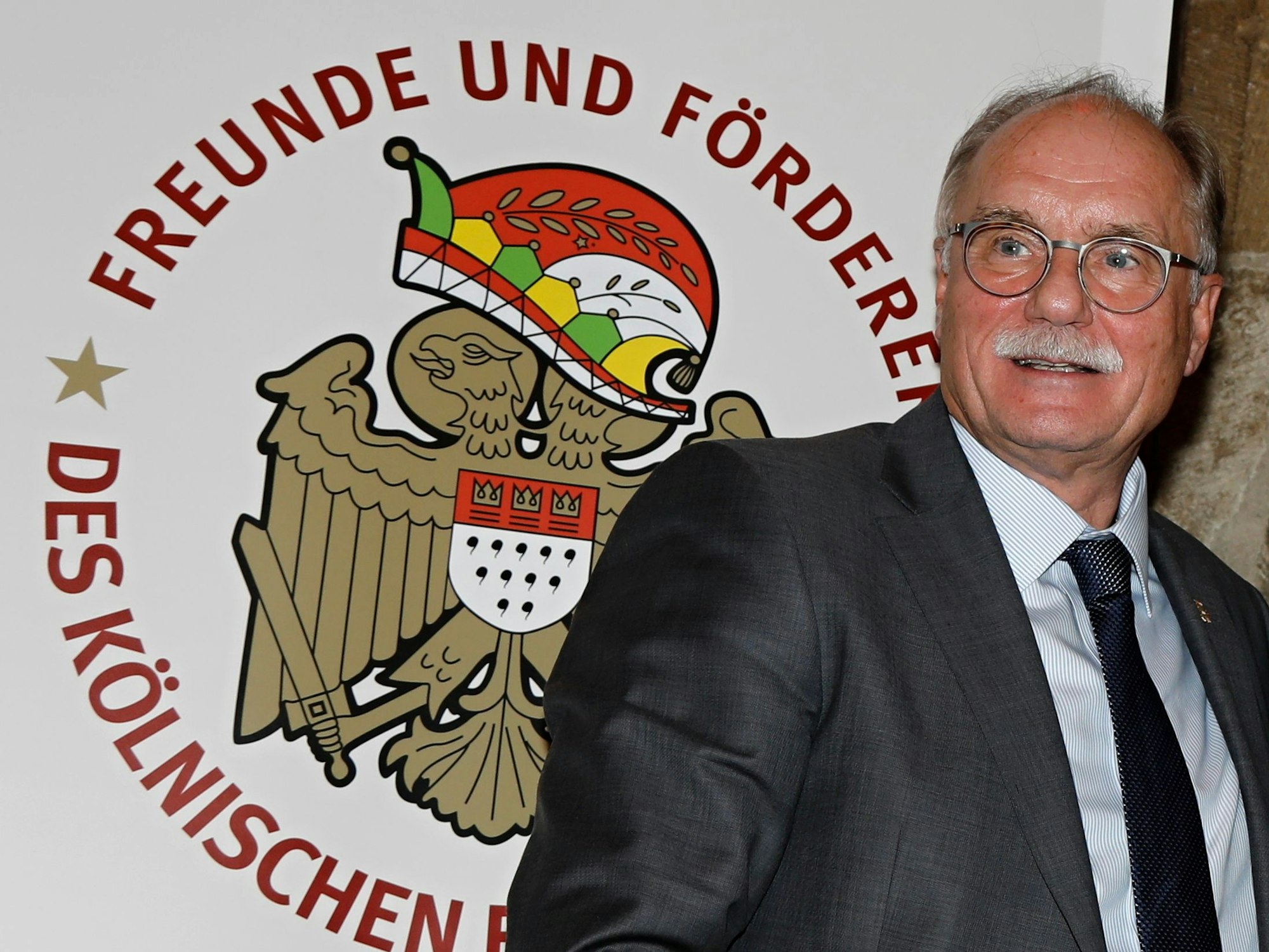 Bernhard Conin steht vor einem Plakat der Freunde und Förderer des Kölnischen Brauchtums.
