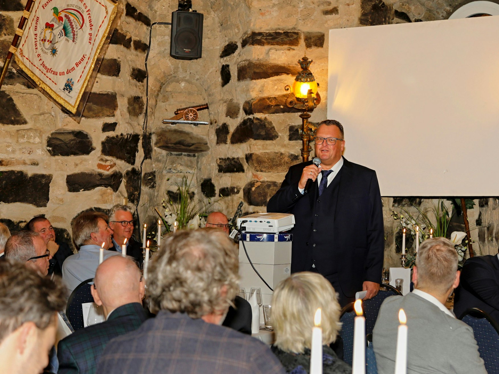 Ein Mann steht mit Mikrofon vor einer Menge von Menschen und hält eine Rede.