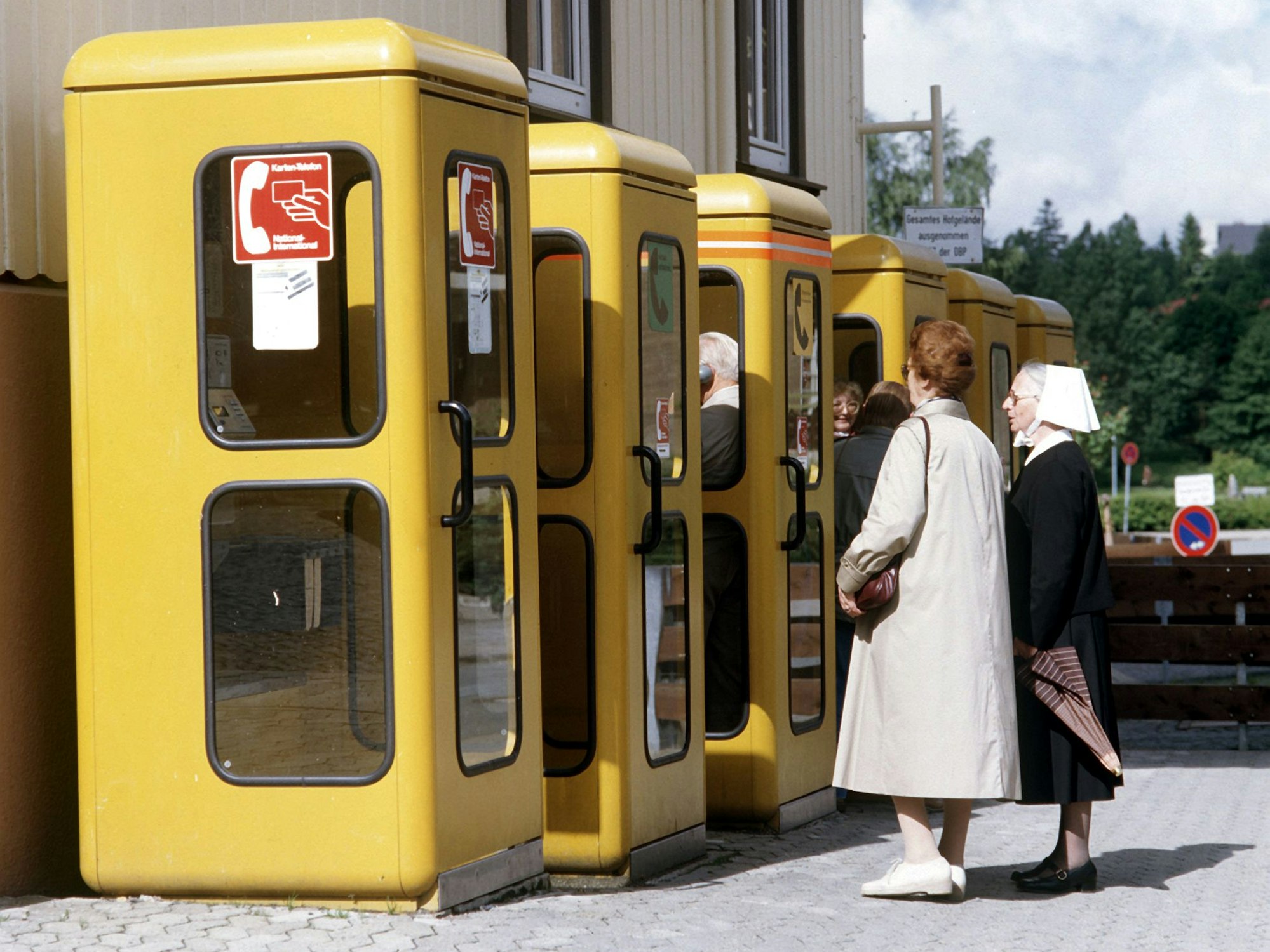 Sechs gelbe Telefonzellen der Deutschen Bundespost mit davor wartenden Kunden, aufgenommen 1985.
