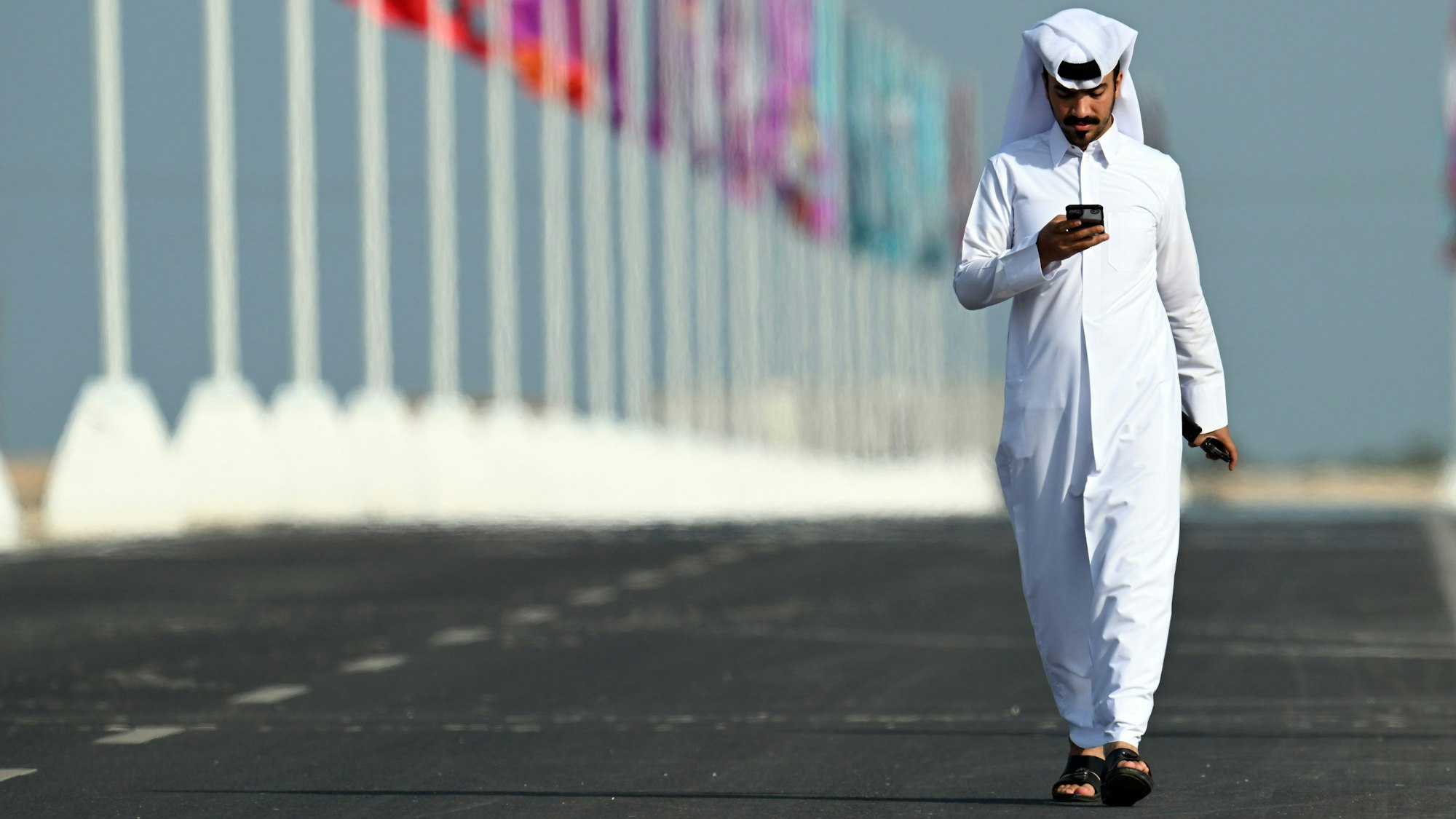 Ein Mann schaut am 17. November 2022 kurz vor dem Start der Fußball-WM in Katar auf sein Handy. Im Hintergrund ist in der Stadt Al Shamal für die WM geschmückt.