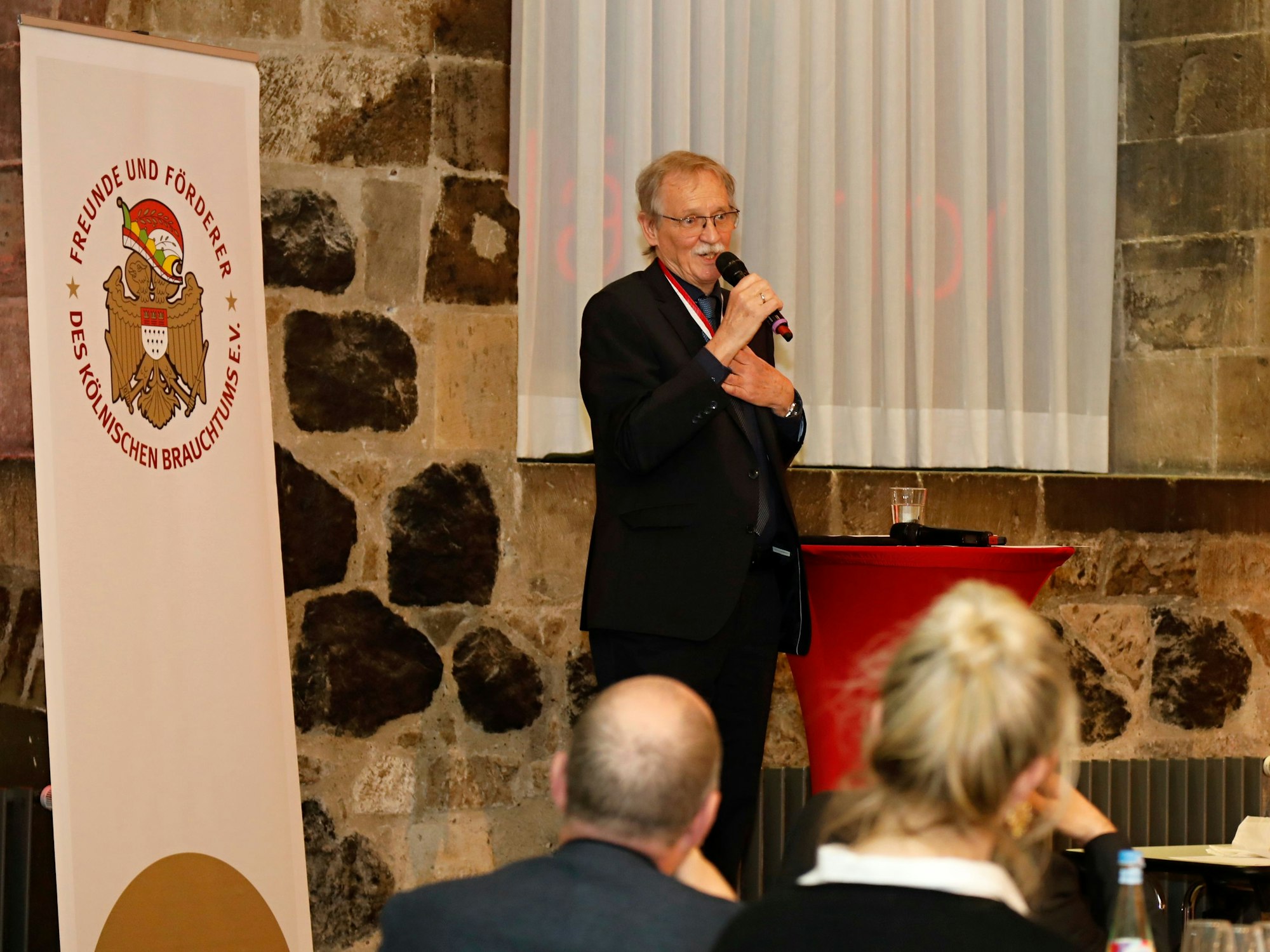 Wolfgang Oelsner steht mit einem Mikrofon auf einer Bühne und spricht zu den Gästen.