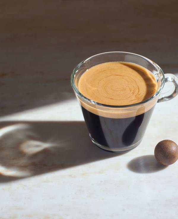 Die gepresste Kaffeekugel als Zero-Waste-Kaffeekapsel liegt neben einer Tasse Kaffee.
