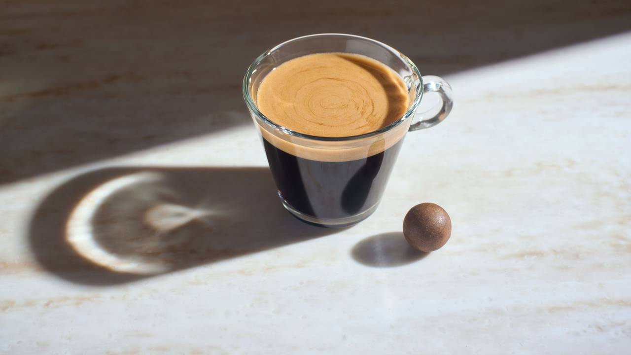 Die gepresste Kaffeekugel als Zero-Waste-Kaffeekapsel liegt neben einer Tasse Kaffee.