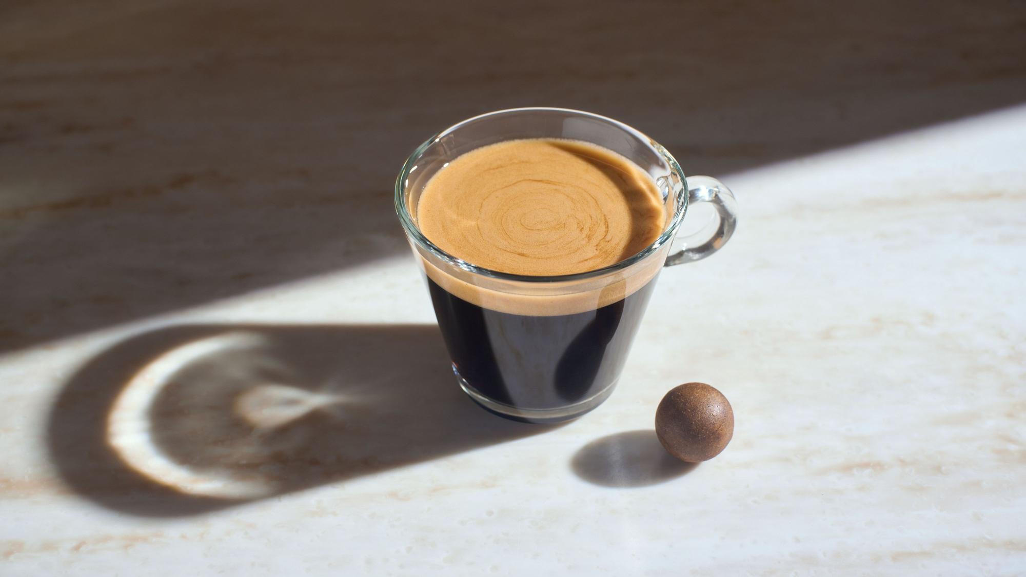 Die gepresste Kaffeekugel als Zero-Waste-Kaffeekapsel liegt neben einer Tasse Kaffee.