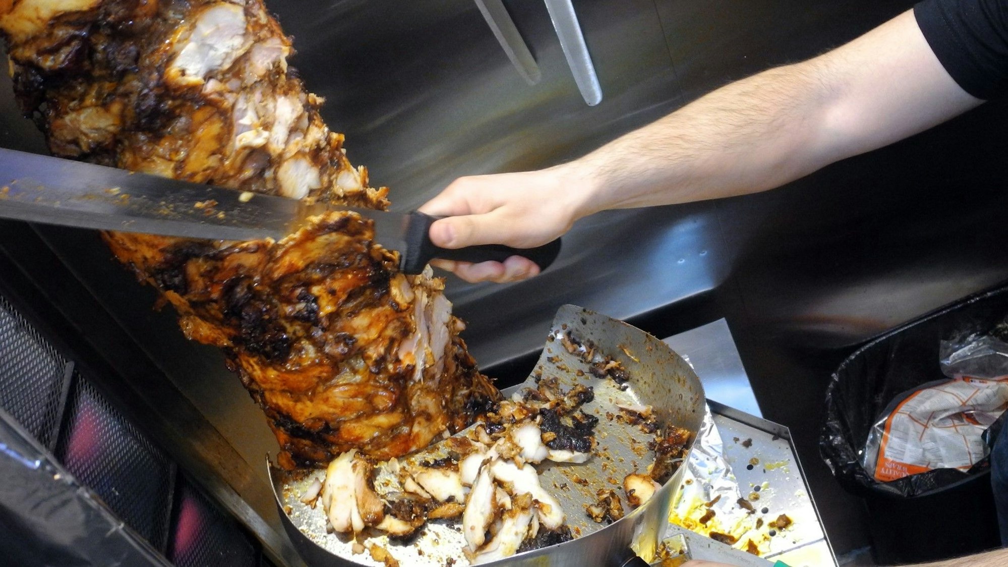 Ein Döner wird zubereitet. Dafür schneidet ein Mann Fleisch von einem Spieß.