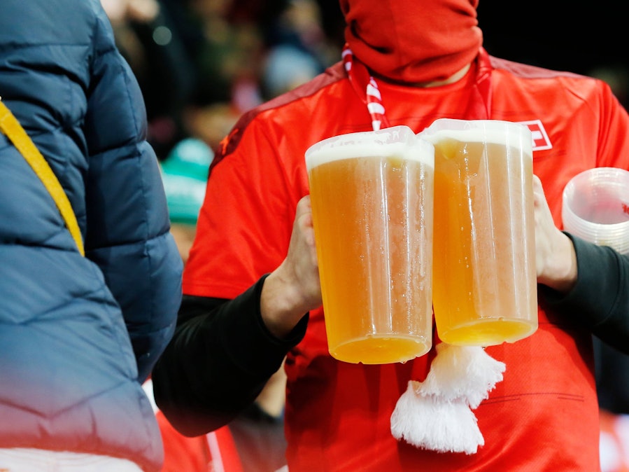 Ein Fan trägt zwei Bier-Becher auf der Tribüne.
