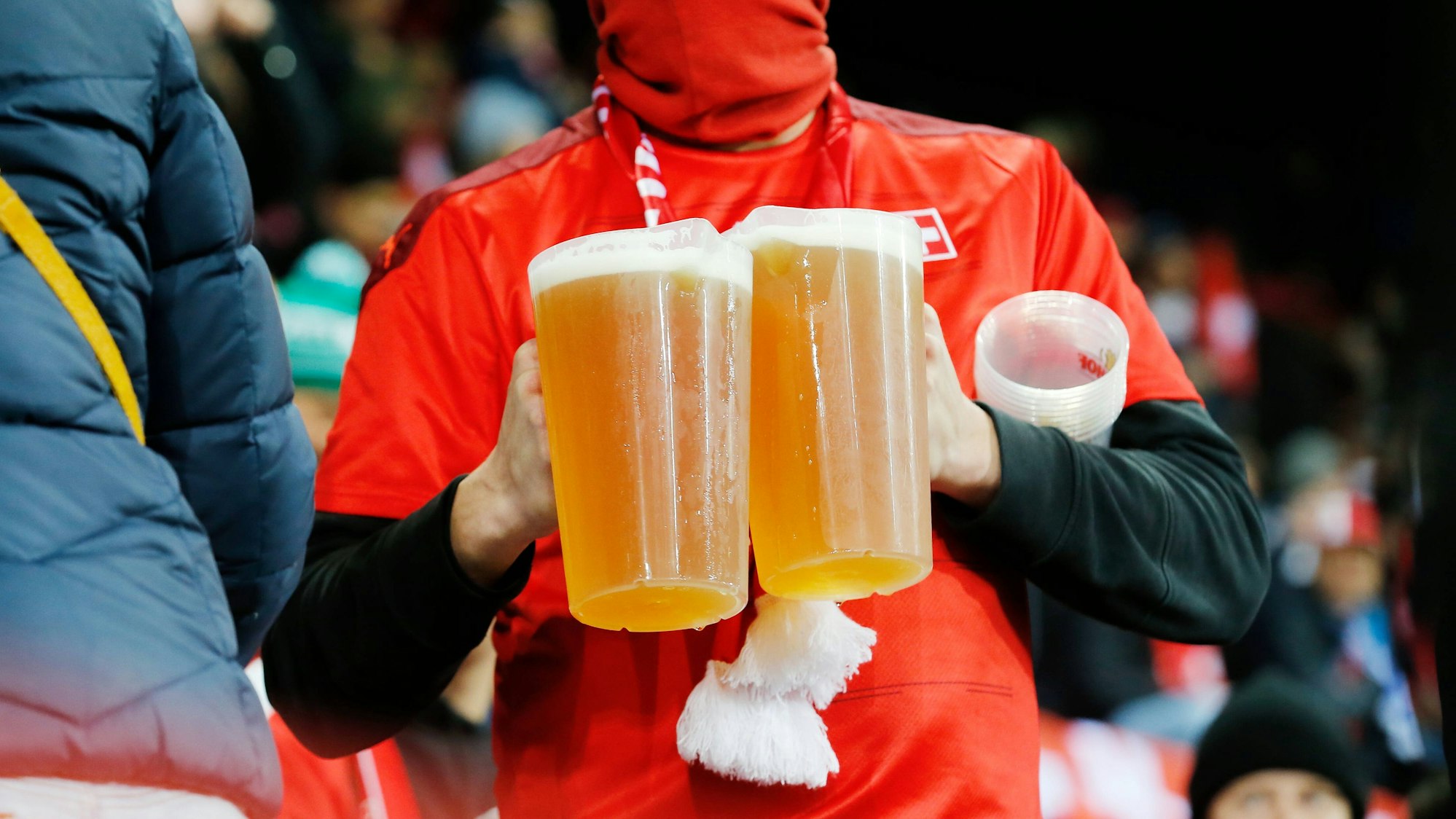 Ein Fan trägt zwei Bier-Becher auf der Tribüne.
