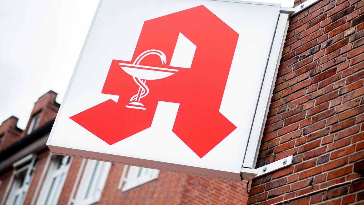 Das Schild für öffentliche Apotheken hängt an einer Hauswand.