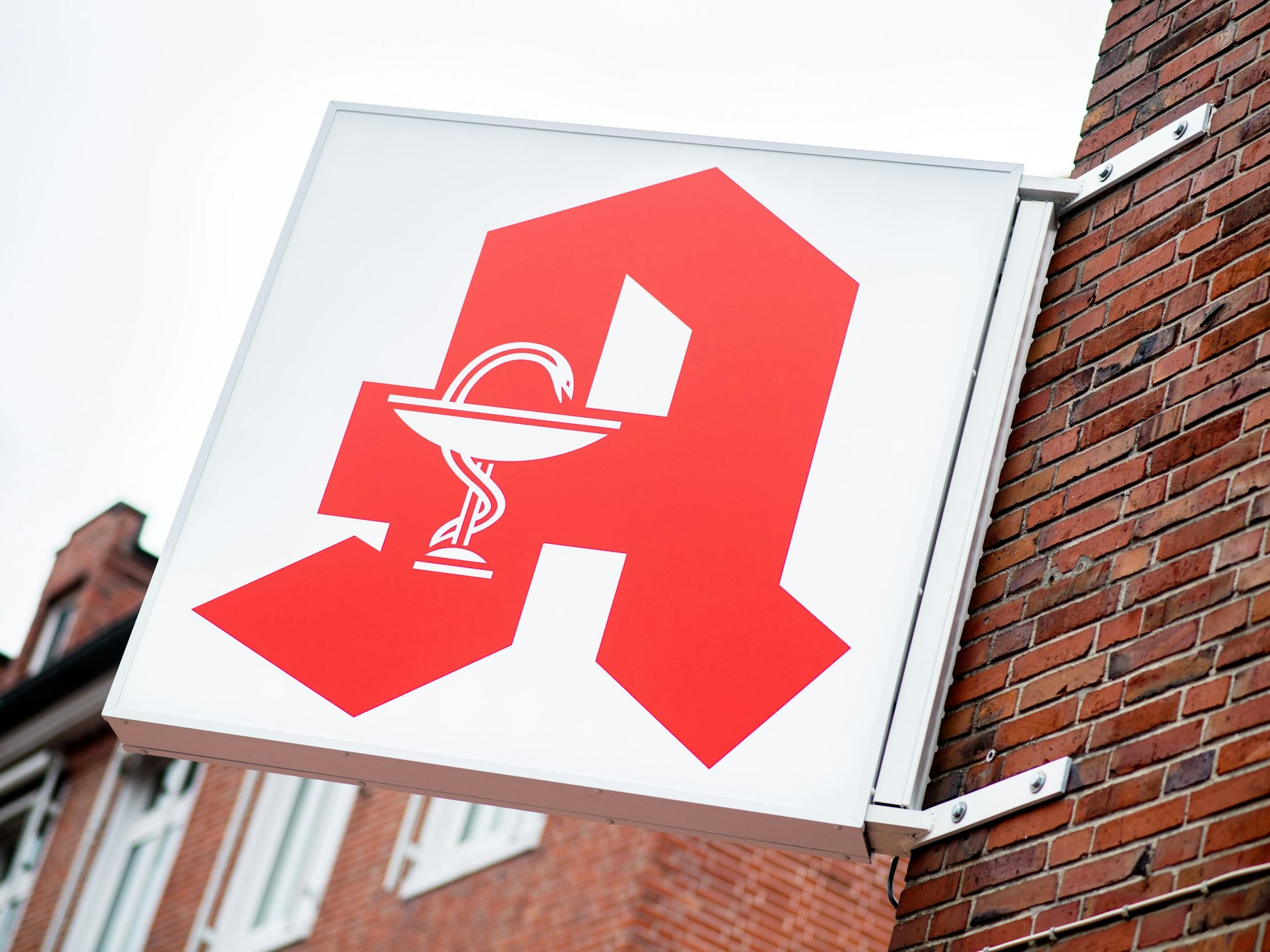 Das Schild für öffentliche Apotheken hängt an einer Hauswand.