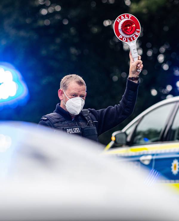 Ein Polizeibeamter steht bei einer Corona-Einreisekontrolle der Bundespolizei an der deutsch-niederländischen Grenze mit einem Polizeianhaltestab und kontrolliert Fahrzeuge im Grenzgebiet.
