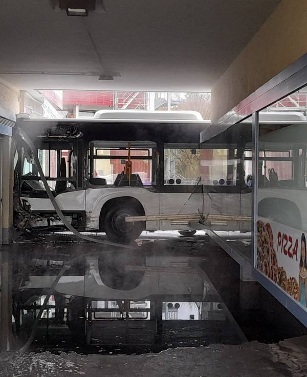 Ein stark beschädigter Bus steht nach einem Unfall an einer ramponierten Ladenzeile.