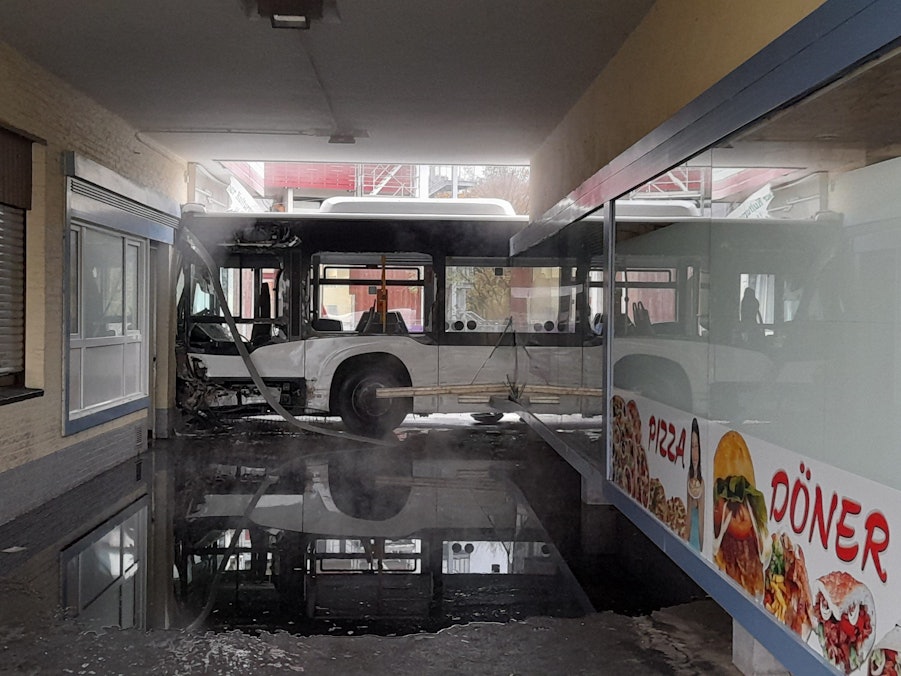 Ein stark beschädigter Bus steht nach einem Unfall an einer ramponierten Ladenzeile.