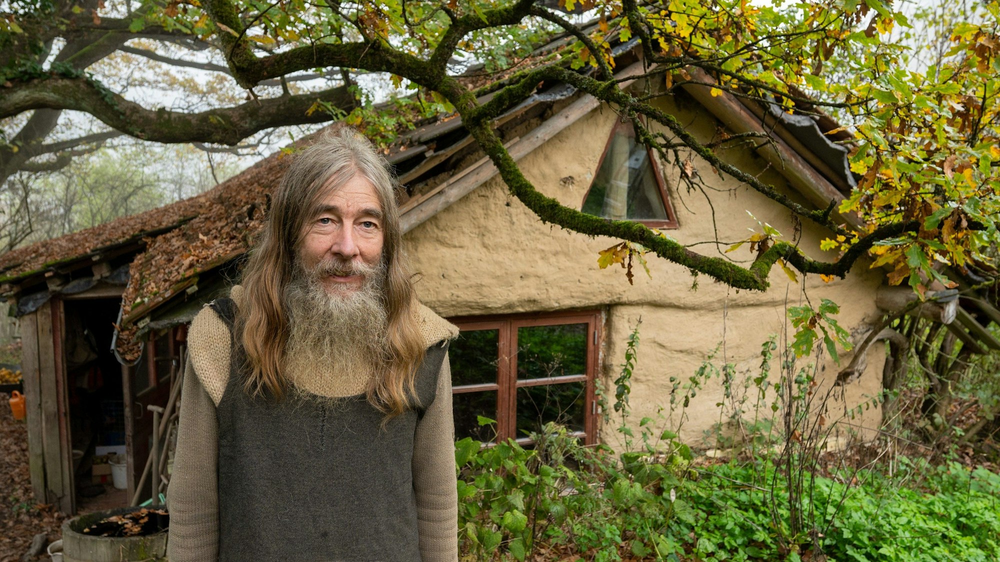Friedmunt Sonnemann steht am frühen Morgen vor seinem Haus. Seit mehr als drei Jahrzehnten lebt er als Aussteiger in einer selbst gebauten Lehmhütte im Wald.