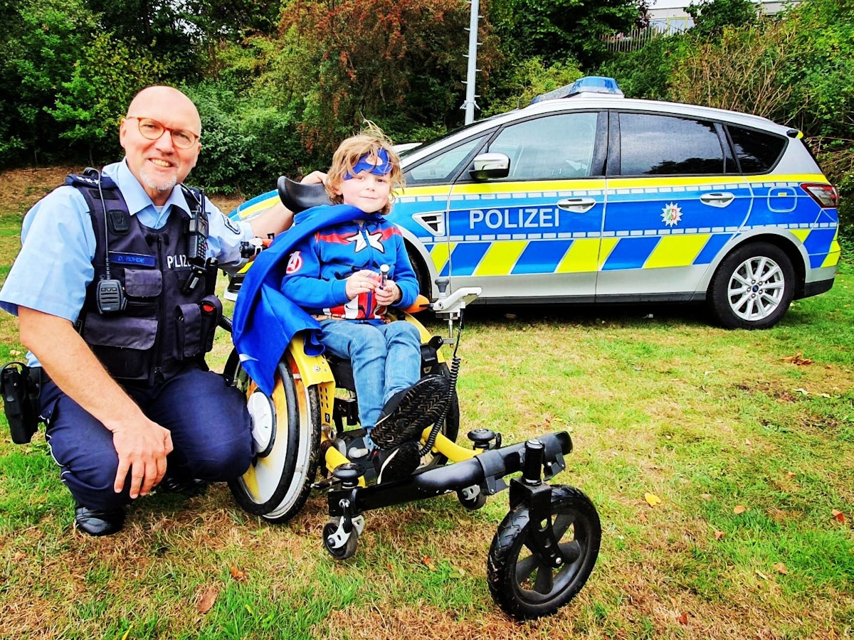 Polizist Dirk Rohde sitzt mit einem schwerkranken Kind auf einem Rasen.