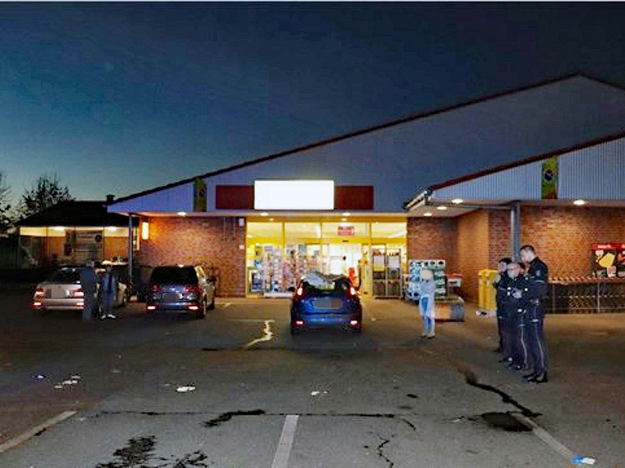 Polizei und einige Autos stehen auf einem Parkplatz vor einem Supermarkt. Der Mann, der hier angefahren wurde, ist mittlerweile tot.