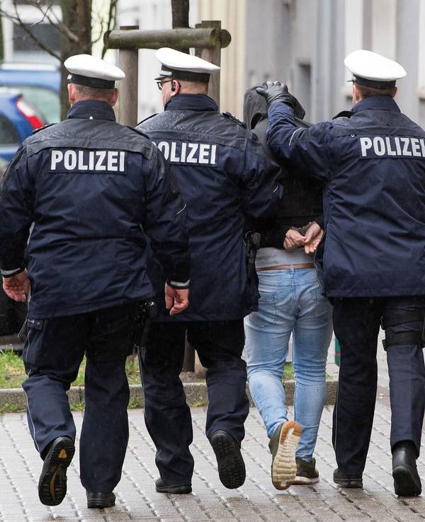 Drei Polizisten führen einen Mann ab.