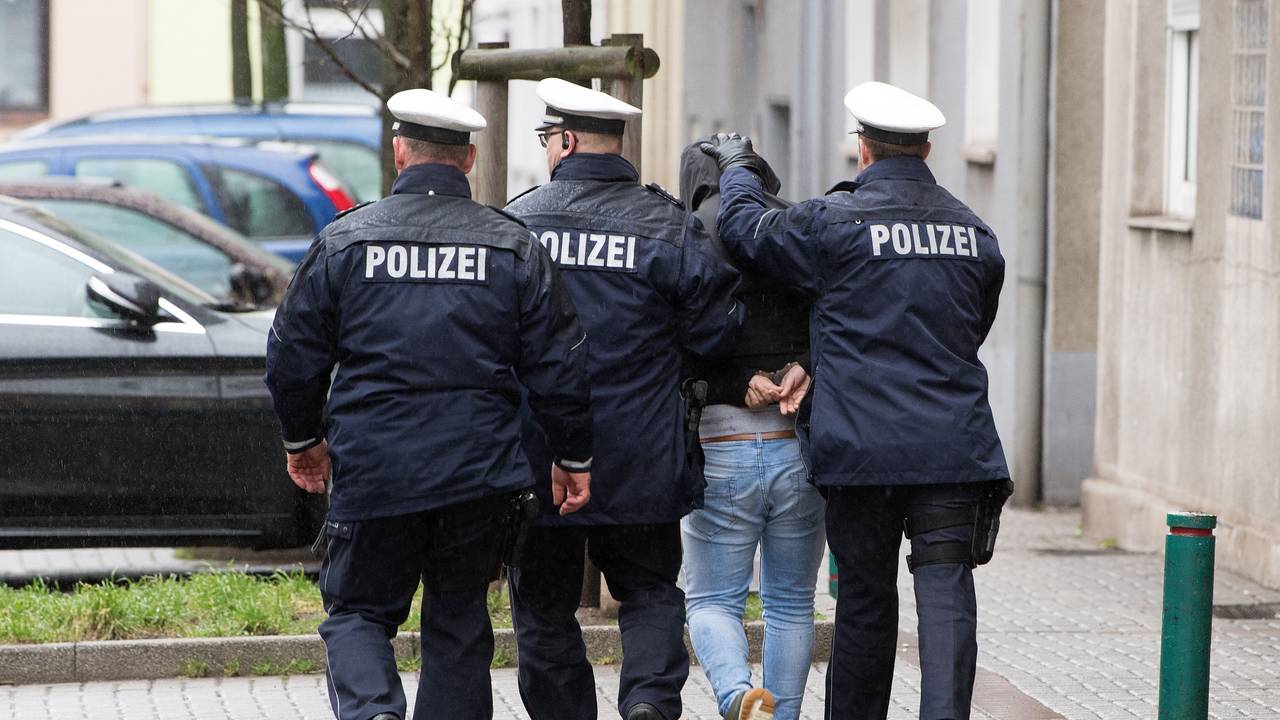 Drei Polizisten führen einen Mann ab.