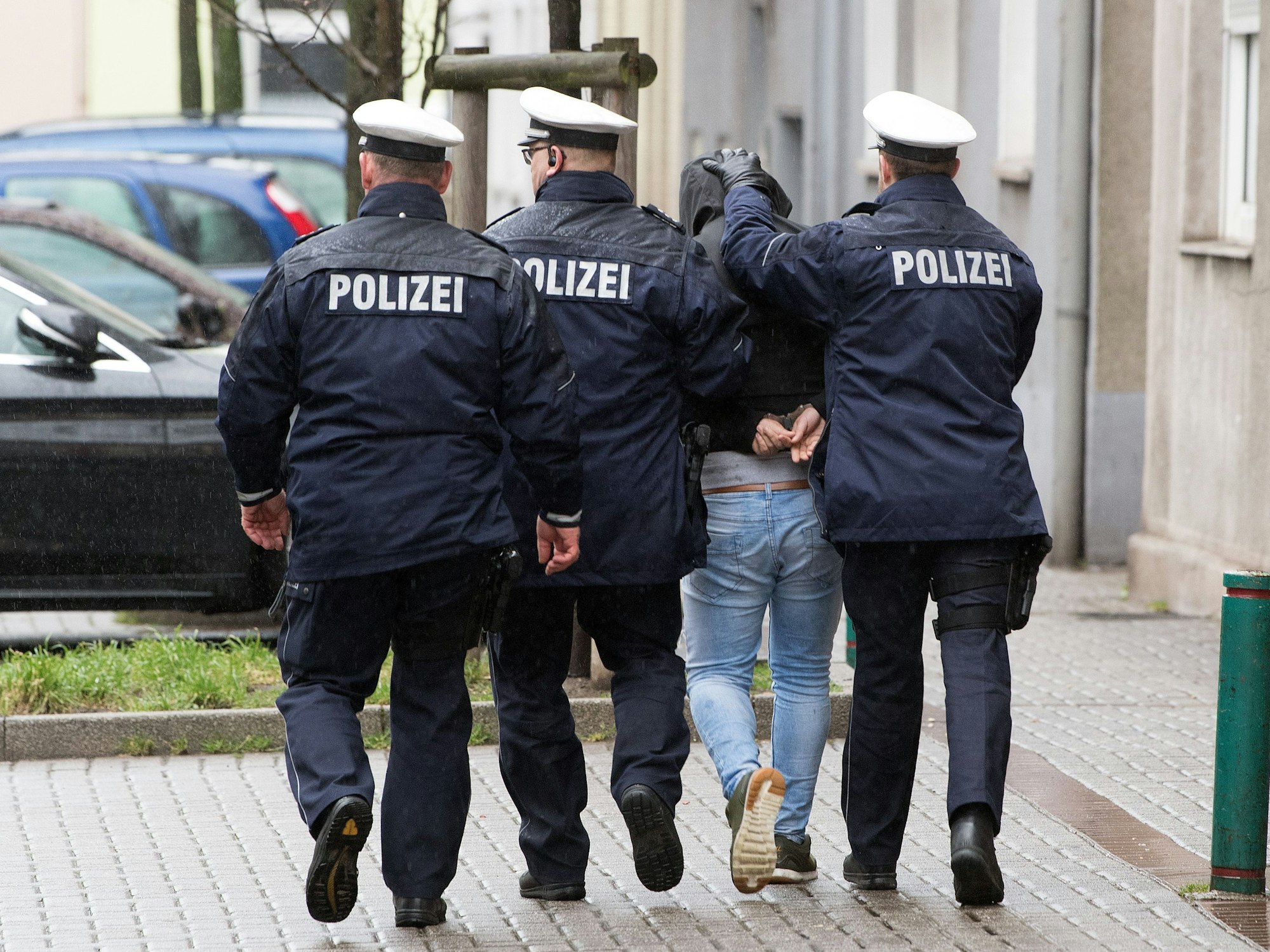 Drei Polizisten führen einen Mann ab.