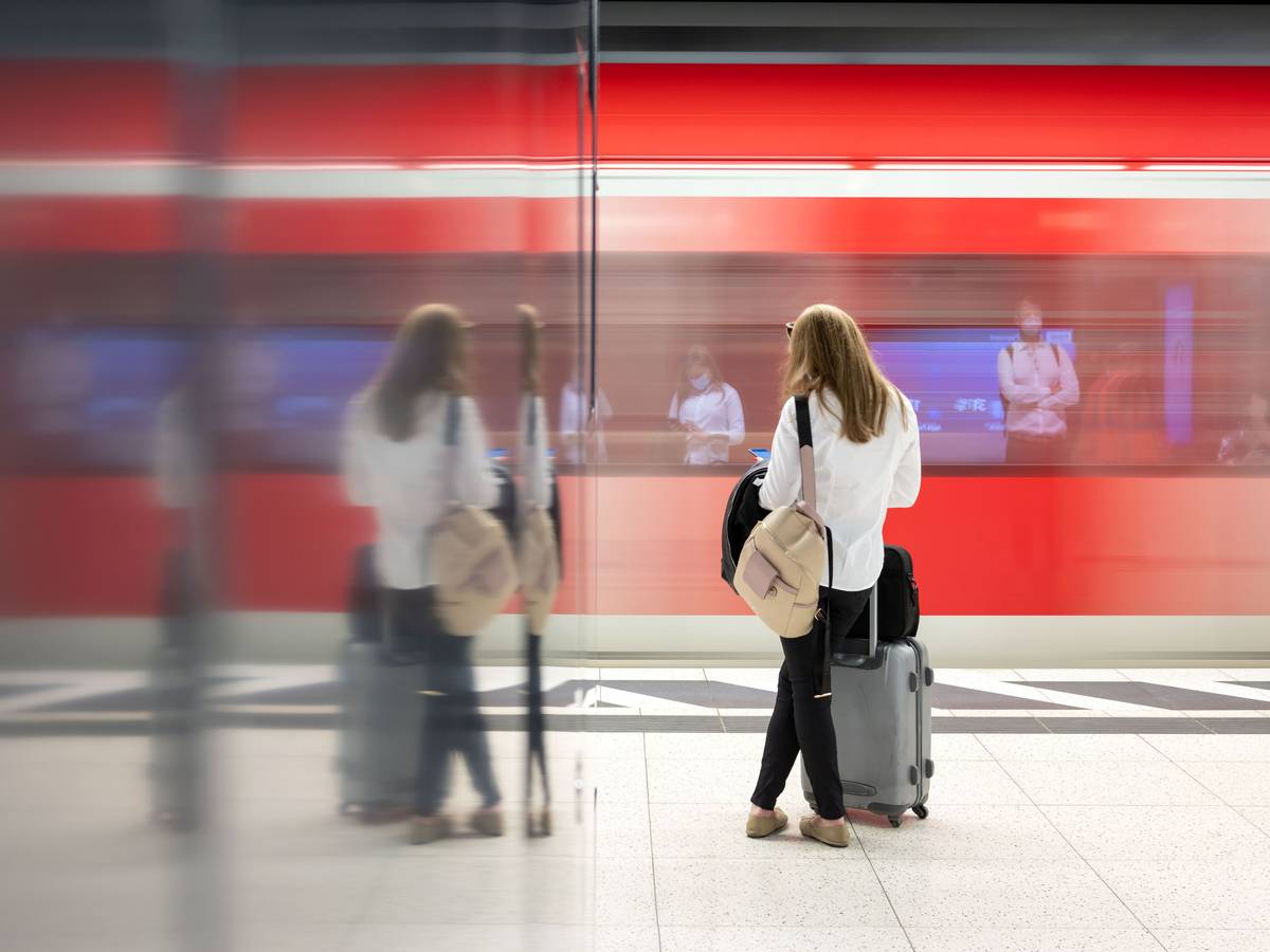 Eine Frau steht an einem Gleis in einem Bahnhof und wartet auf einen Zug.