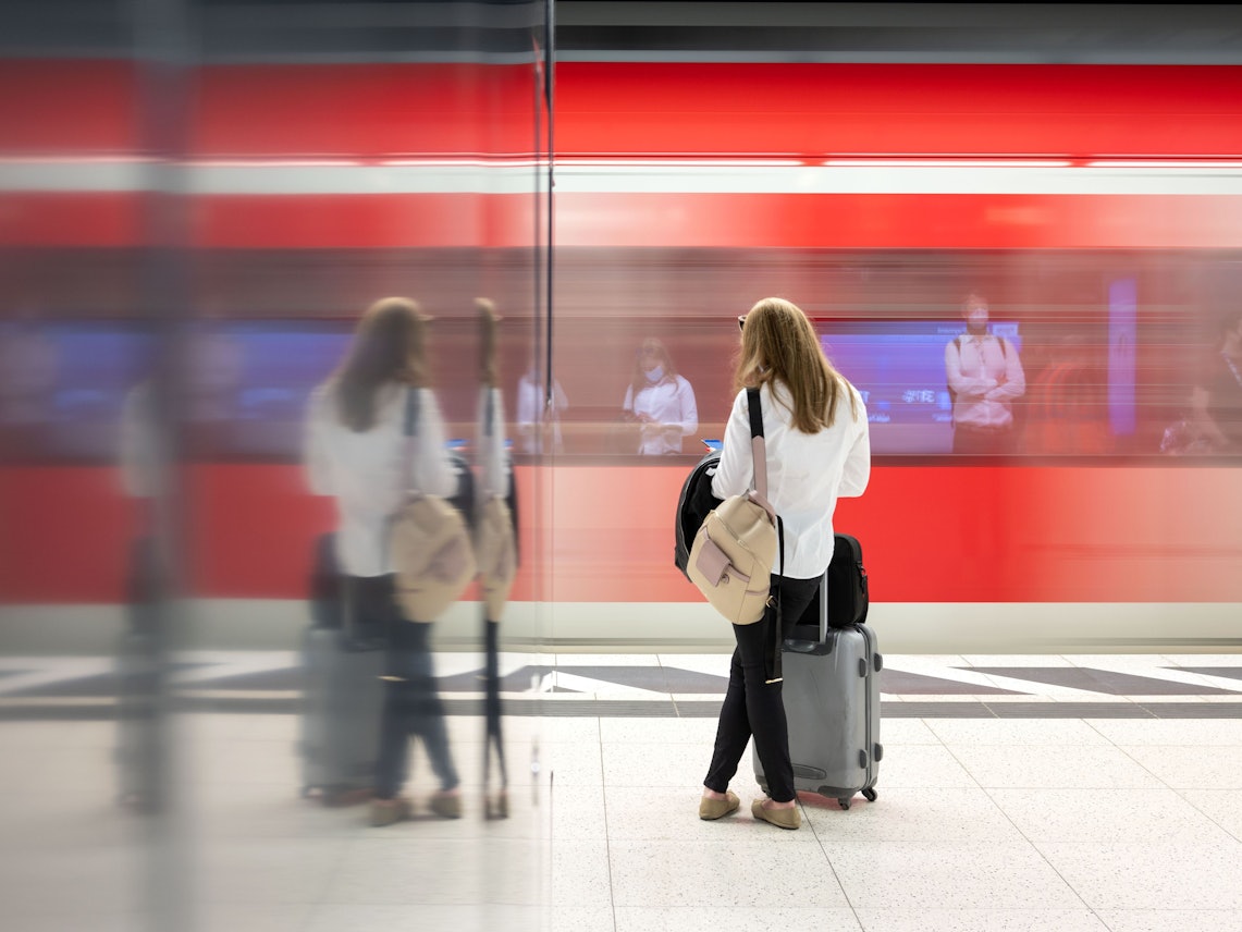 Eine Frau steht an einem Gleis in einem Bahnhof und wartet auf einen Zug.