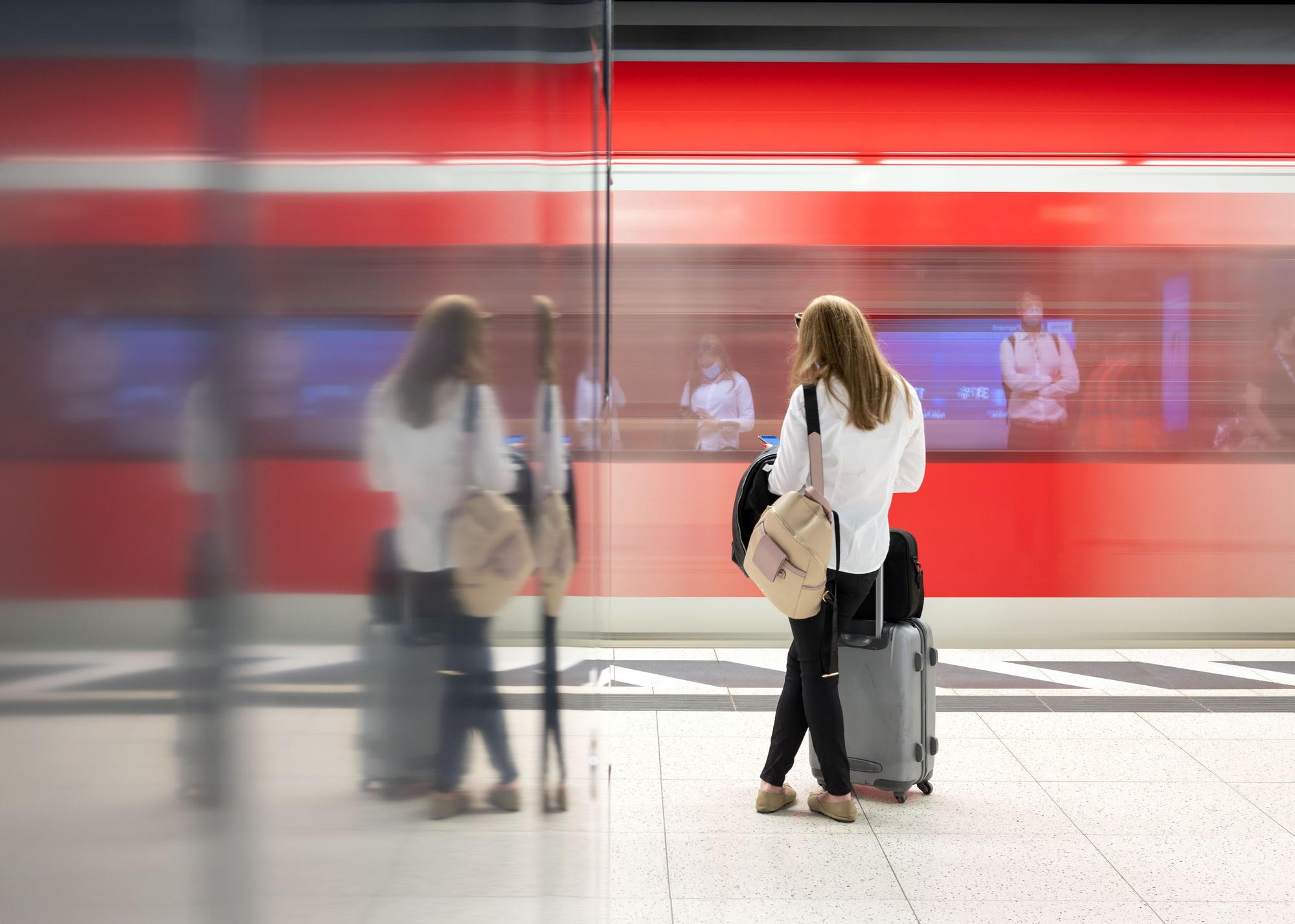 Eine Frau steht an einem Gleis in einem Bahnhof und wartet auf einen Zug.
