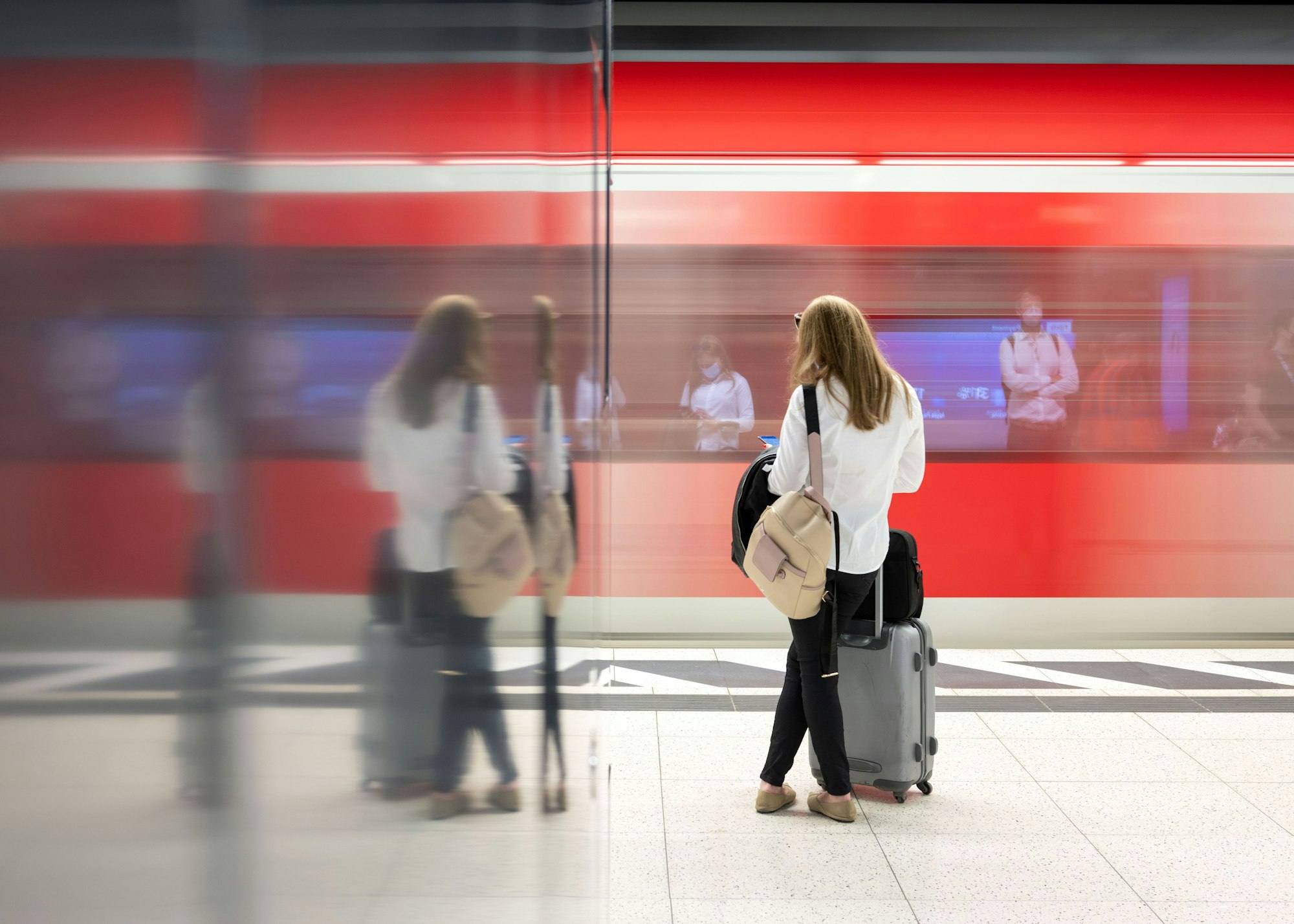 Eine Frau steht an einem Gleis in einem Bahnhof und wartet auf einen Zug.