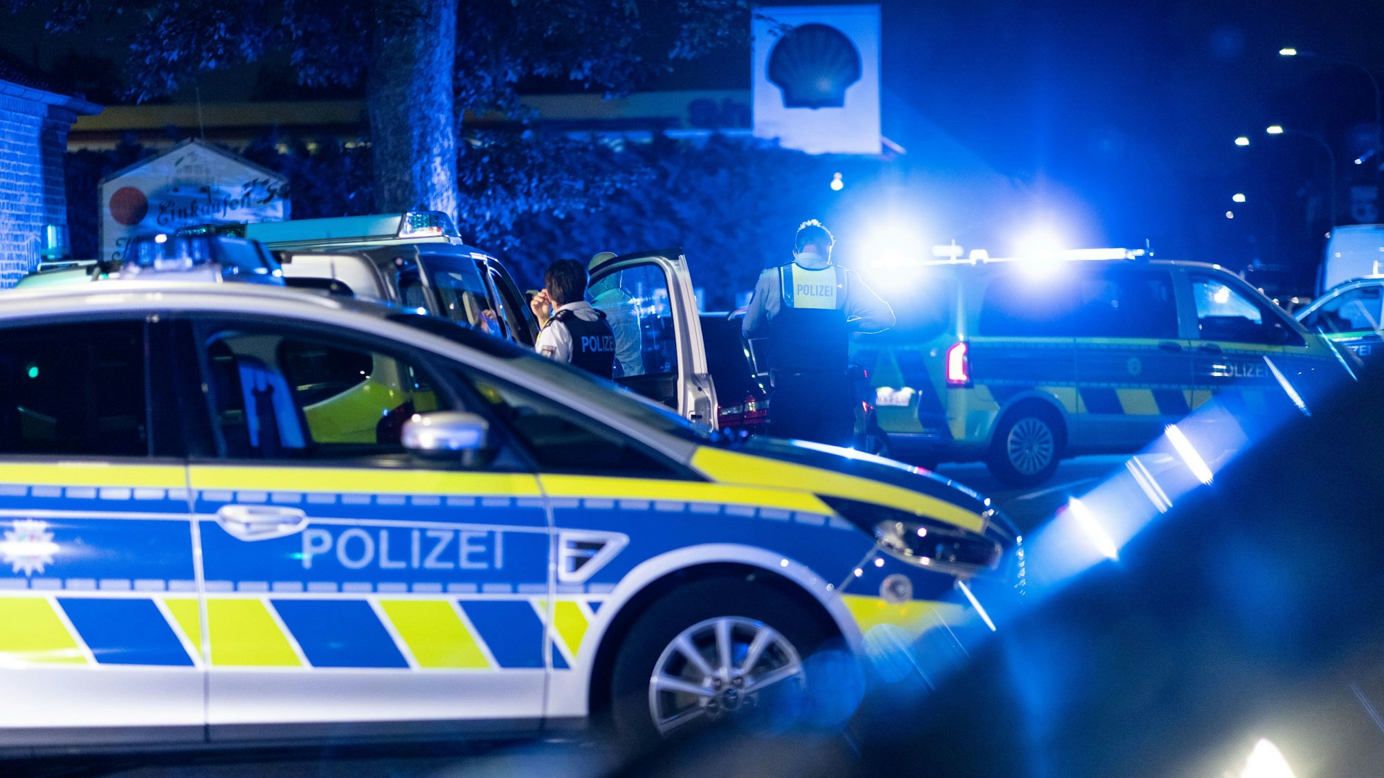 Einsatzkräfte der Polizei stehen vor einer Tankstelle.