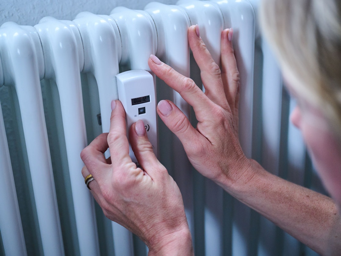 Eine Frau kontrolliert einen Heizkostenverteiler an der Heizung.