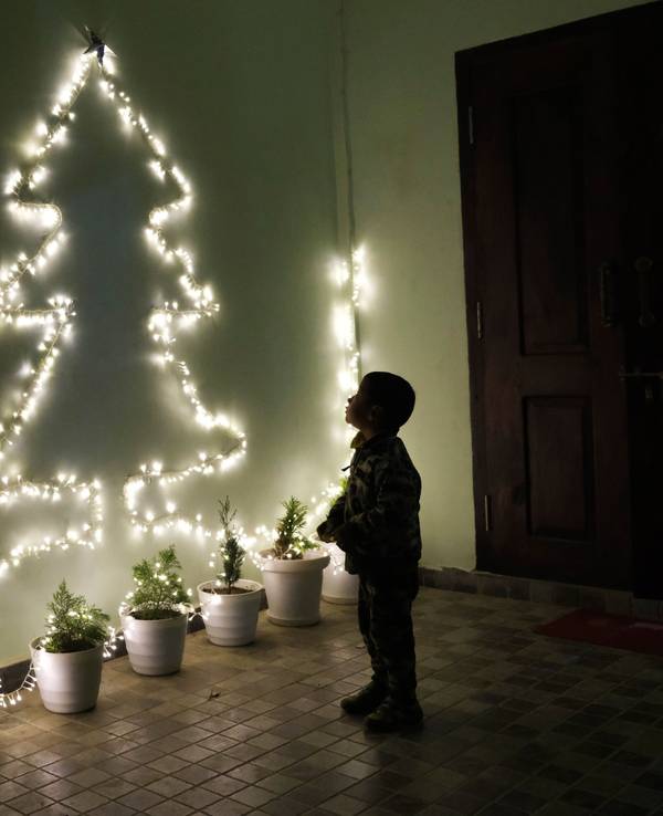 Ein Kind betrachtet an einer Wand eine Lichterkette in Form eines Weihnachtsbaumes.