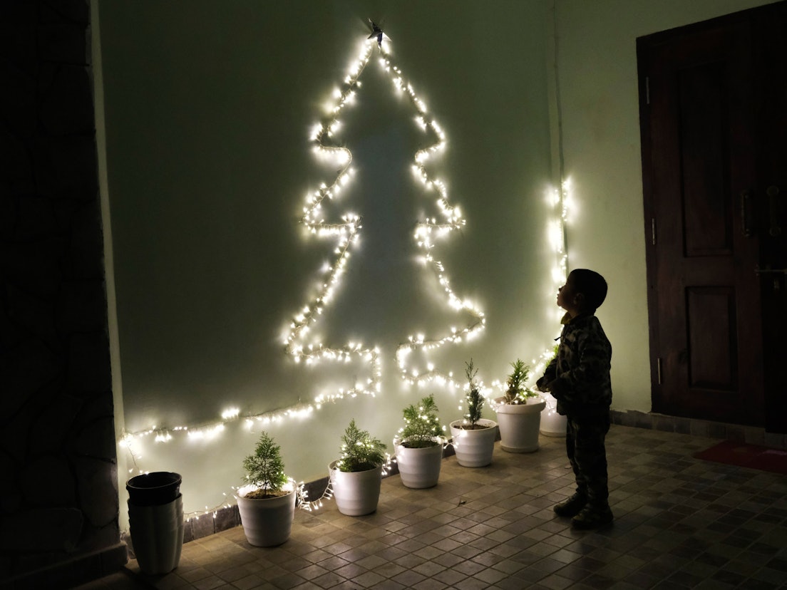 Ein Kind betrachtet an einer Wand eine Lichterkette in Form eines Weihnachtsbaumes.