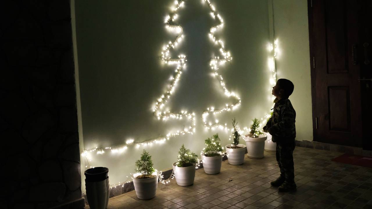 Ein Kind betrachtet an einer Wand eine Lichterkette in Form eines Weihnachtsbaumes.