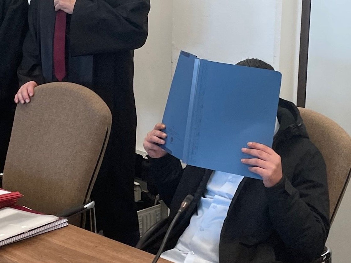 Der Angeklagte hält sich einen Ordner vor das Gesicht.