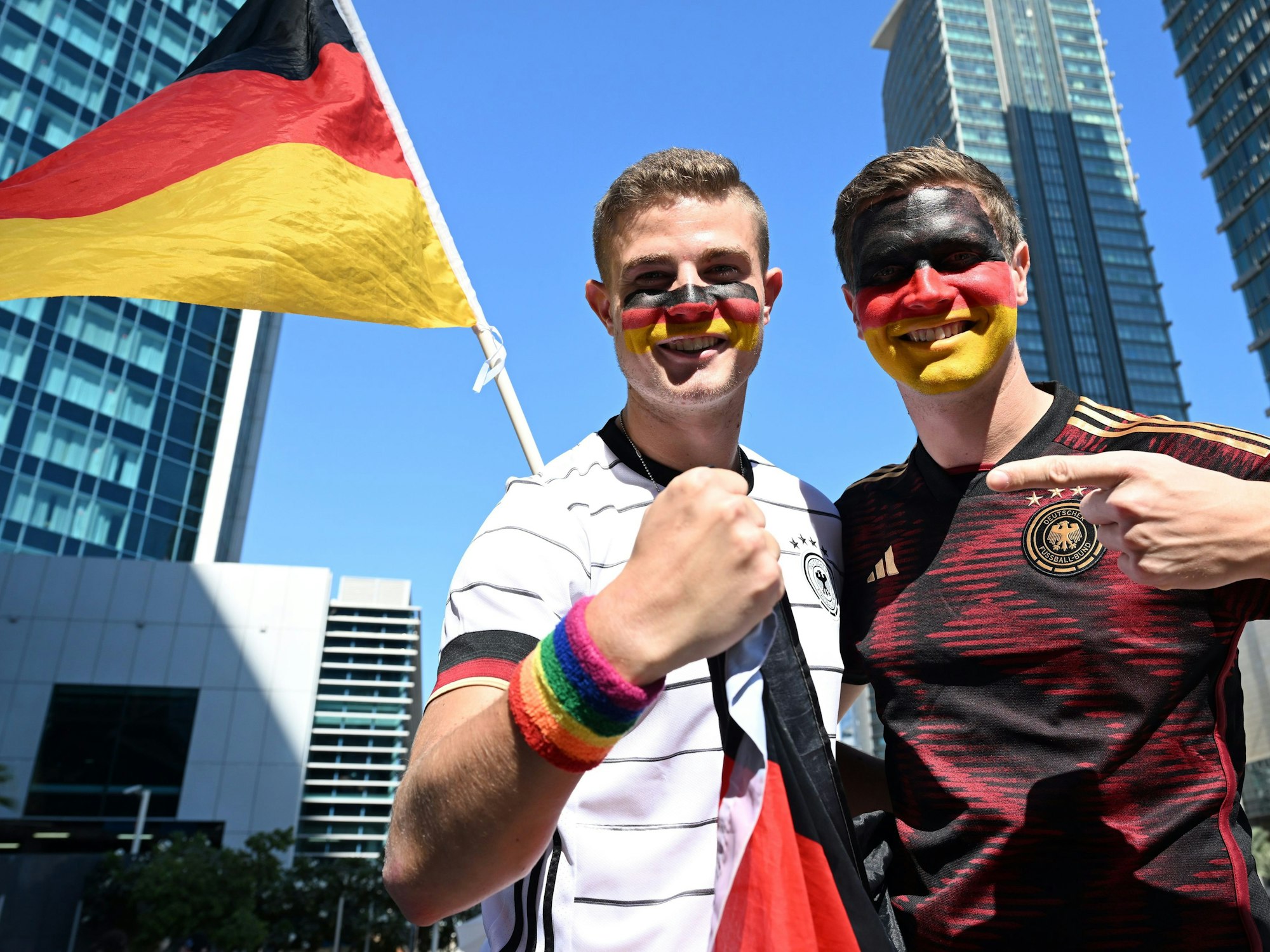 Bengt Kunkel hält sein Armband in Regenbogenfarben in die Kamera, neben ihm steht sein Bruder Jan. Beide haben ihre Gesichter in den Deutschland-Farben bemalt.