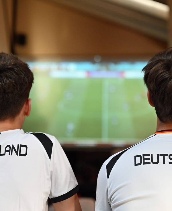 Zwei junge Männer schauen im Deutschland-Trikot Fußball im TV.