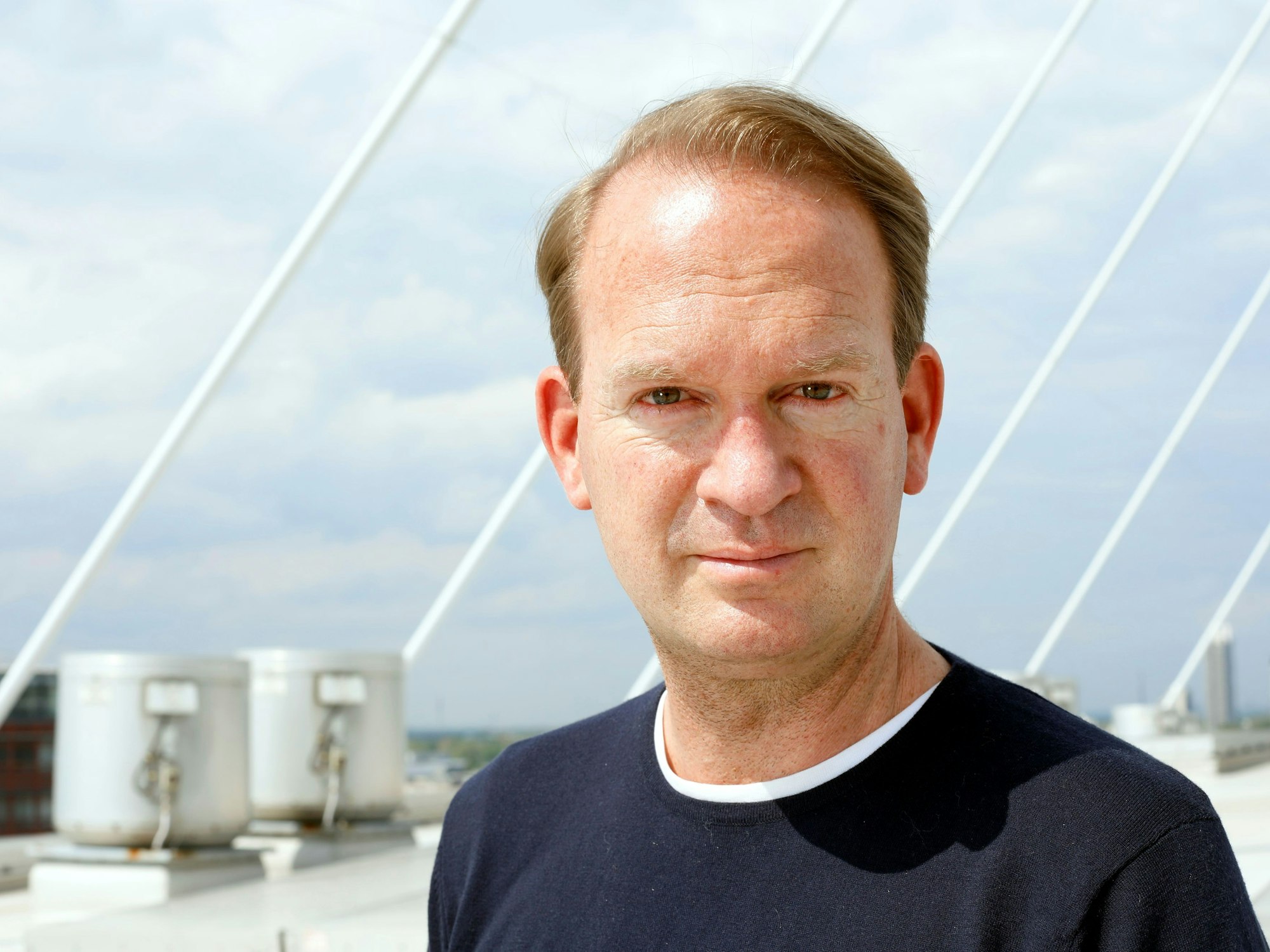 Stefan Löcher steht auf dem Dach seiner Lanxess-Arena und blickt in die Kamera.