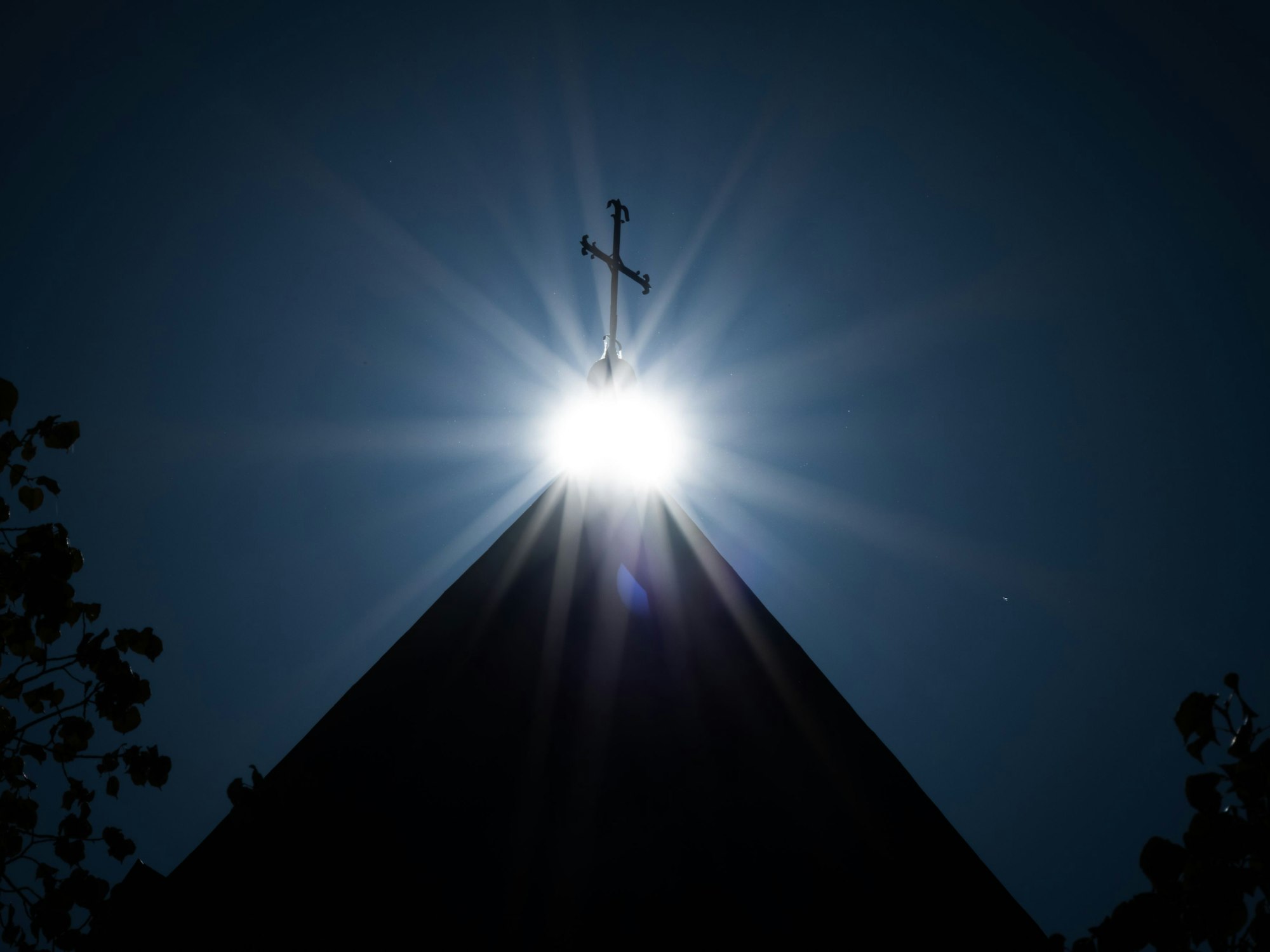 Die Sonne strahlt unter einem Kreuz auf dem Dom Osnabrück.