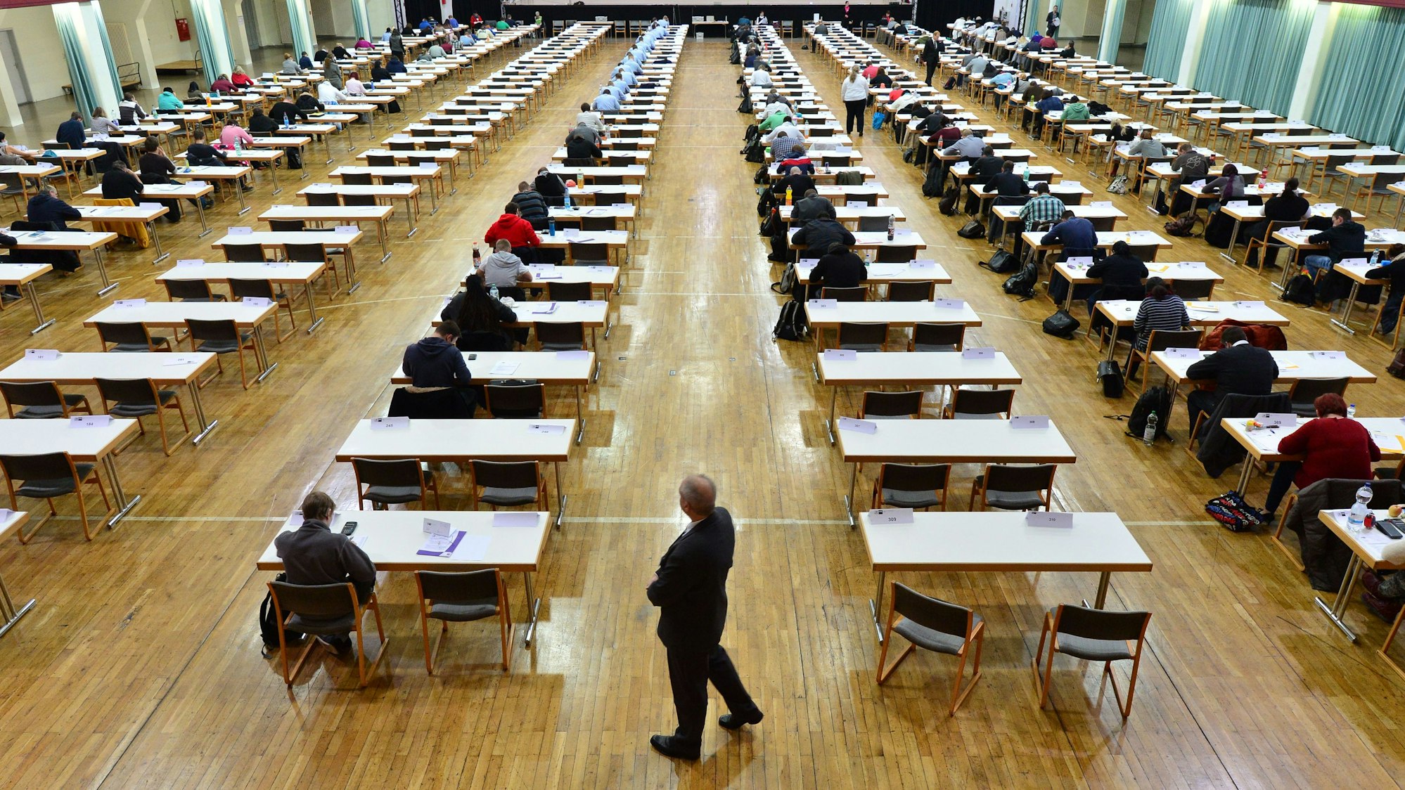 Rund 200 Jugendliche sitzen in einer Halle über ihrer Abschlussprüfung.