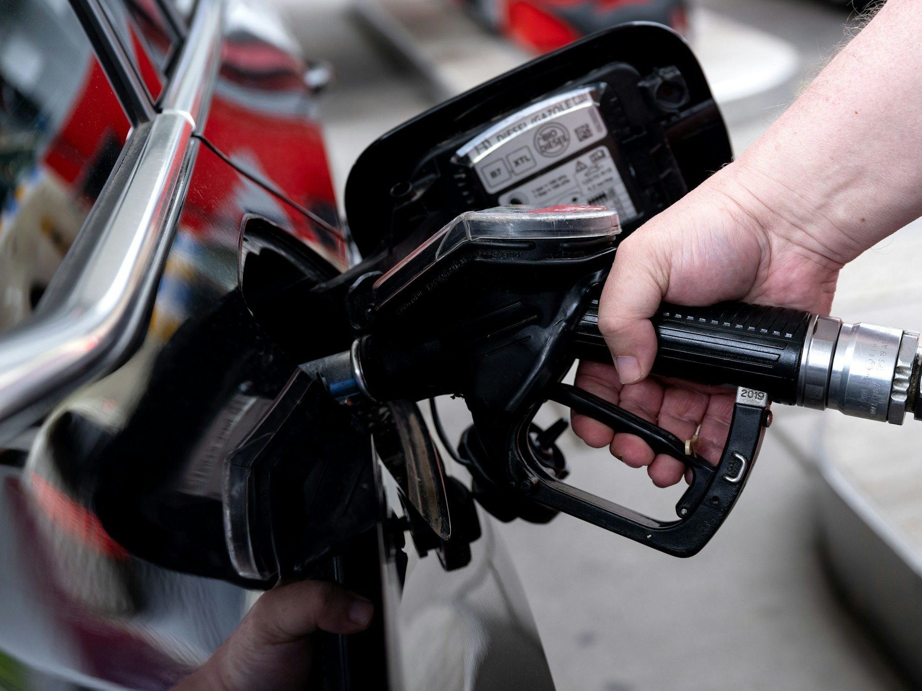 Ein Mann hält eine Zapfpistole an einer Tankstelle in der Hand und betankt sein Auto.