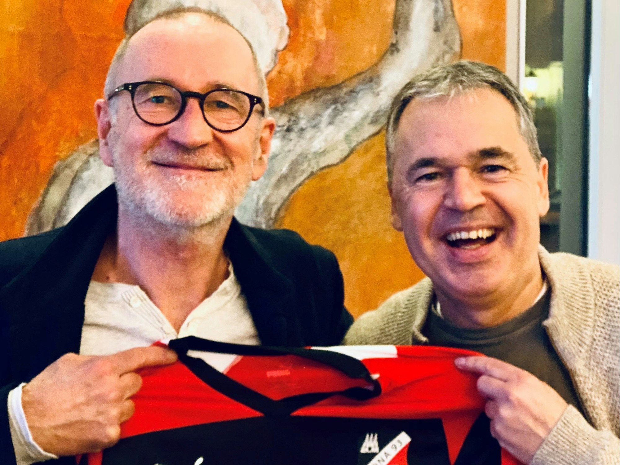Peter Lohmeyer und Andreas Rettig lächeln mit einem Trikot in die Kamera.