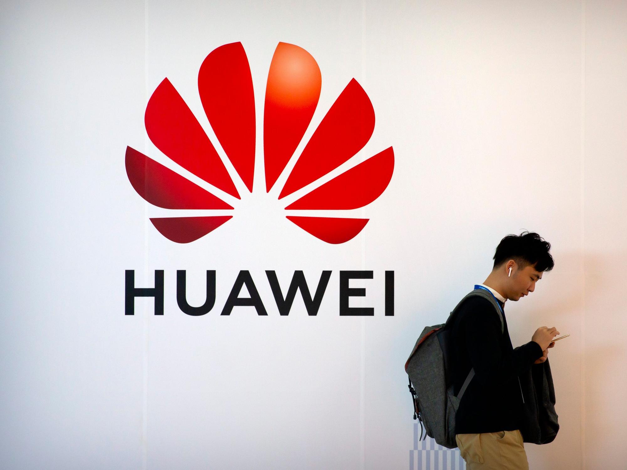 Ein Mann tippt auf seinem Smartphone, während er auf der Fachmesse PT Expo in der Nähe einer Werbetafel für die chinesische Technologiefirma Huawei steht.
